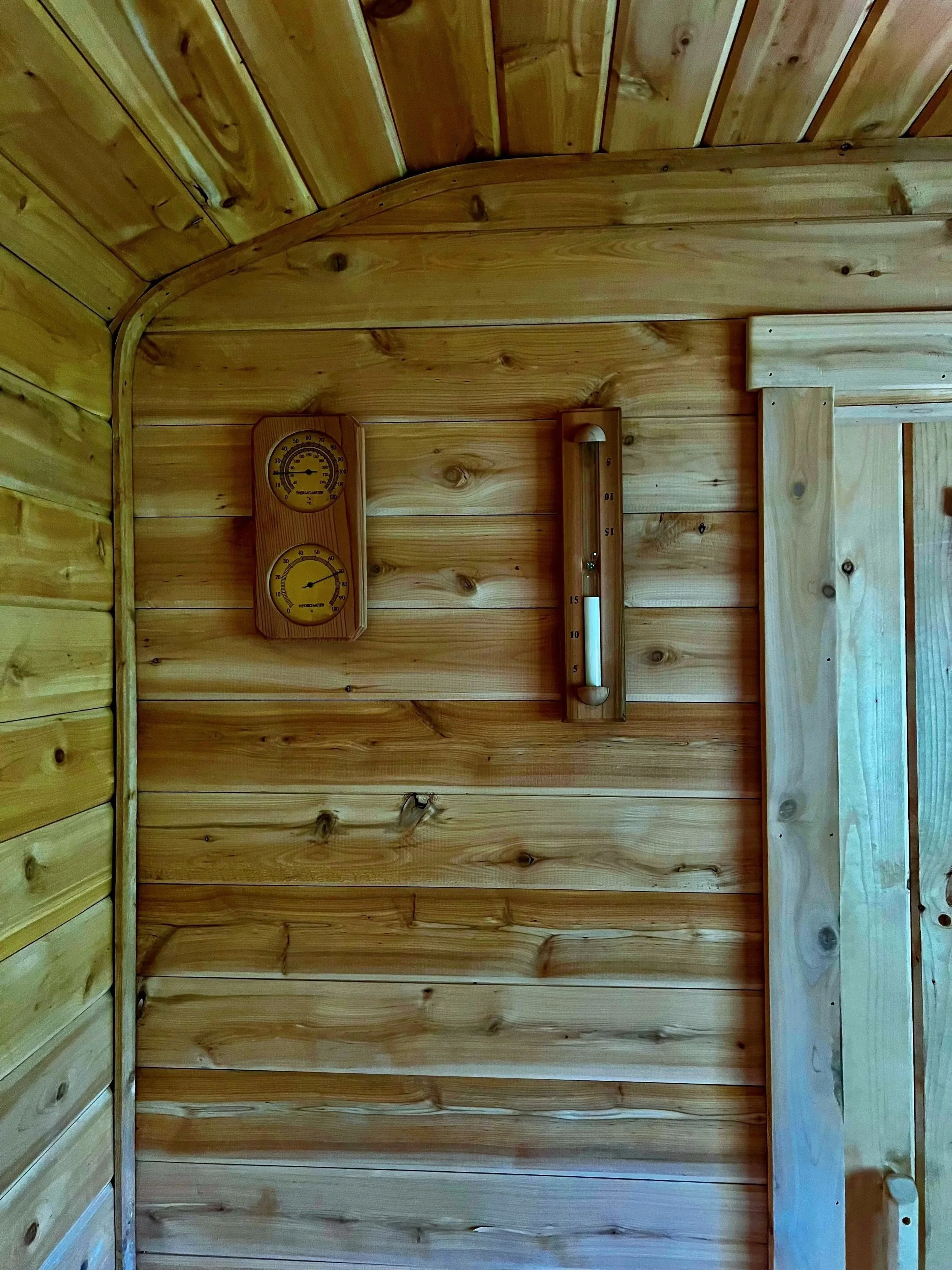 Sauna wall detail showing analog thermometer and humidity gauge mounted on tongue and groove wall.