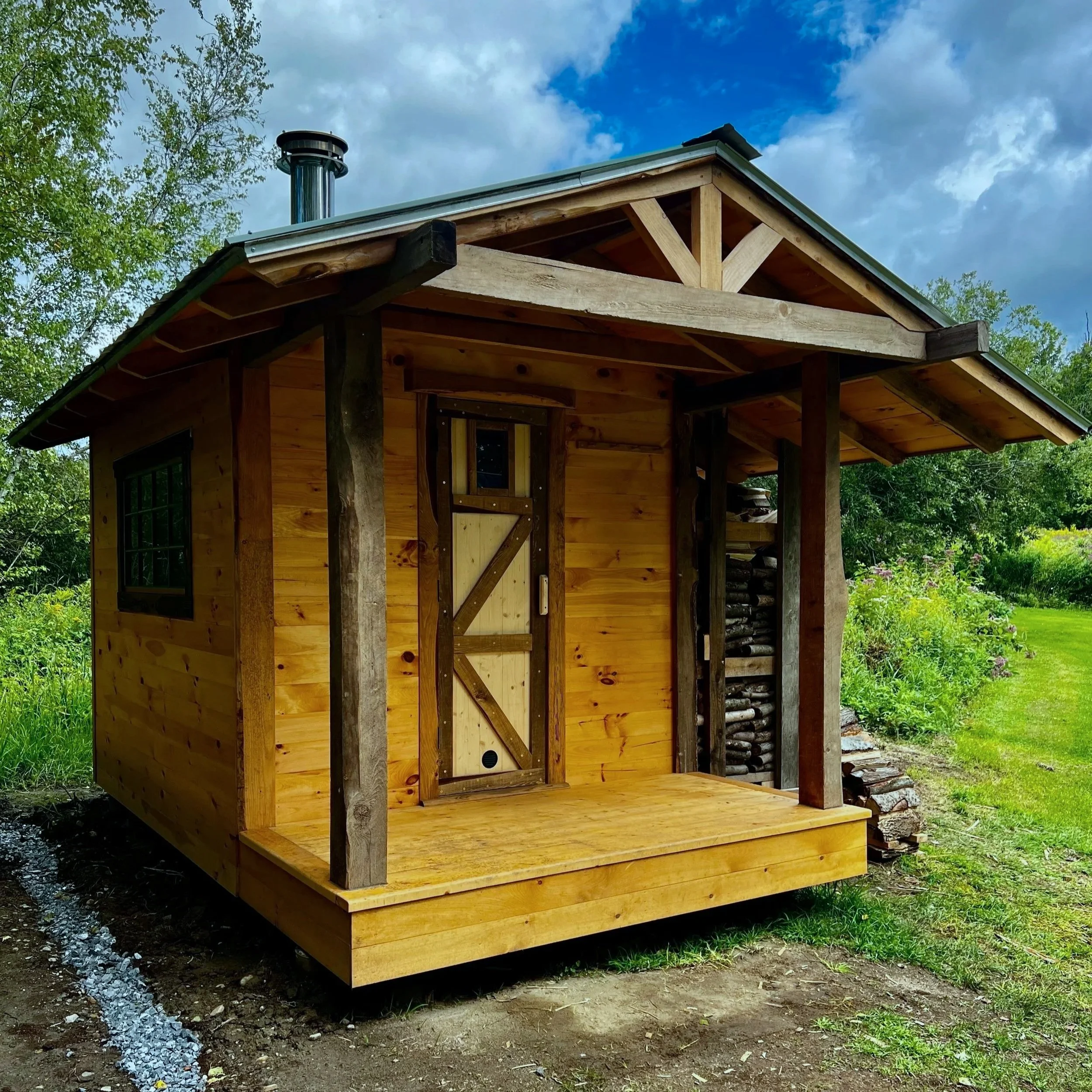 Custom outdoor sauna with covered entry porch by Hot Bird Saunas, set in a Vermont landscape surrounded by greenery.