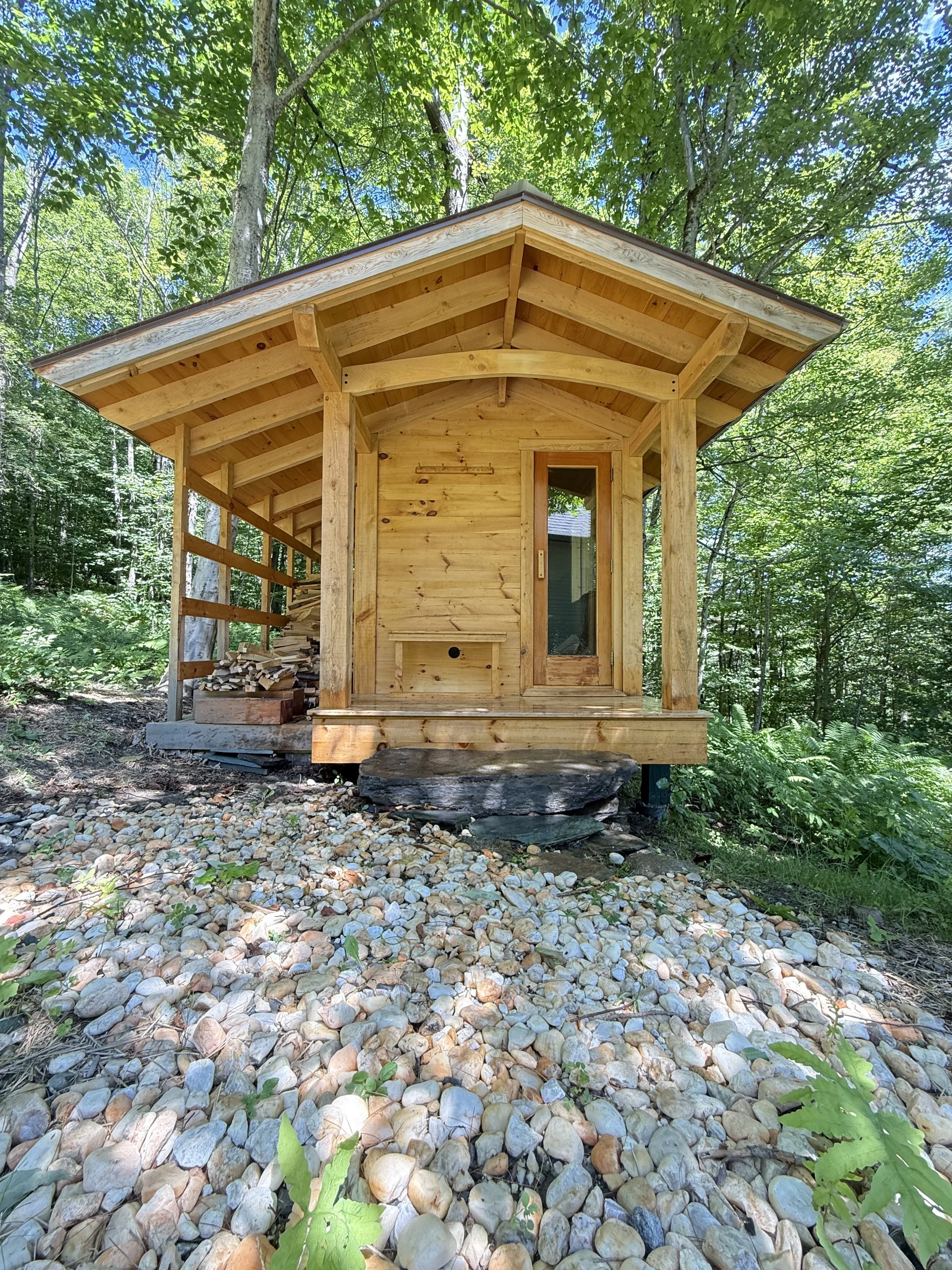 Custom outdoor sauna with covered entry porch by Hot Bird Saunas, sited among trees and stone in a Vermont forest environment.