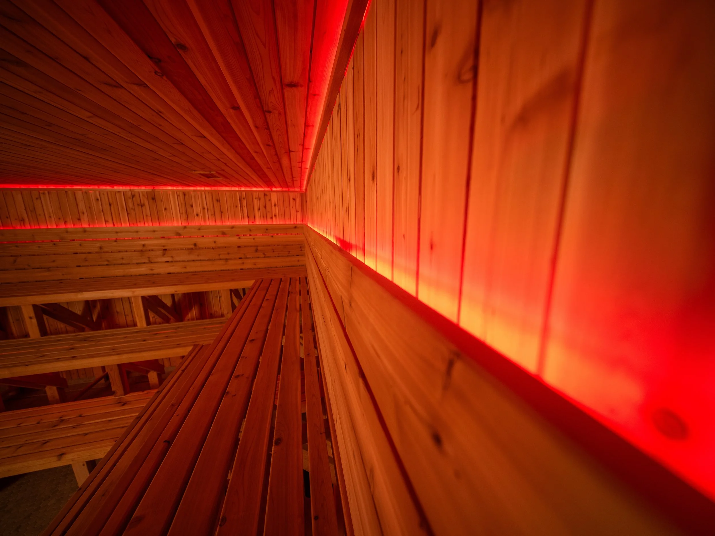 Detail view of a custom sauna interior highlighting cedar tongue and groove walls and red LED lighting integrated along the ceiling and wall edges.