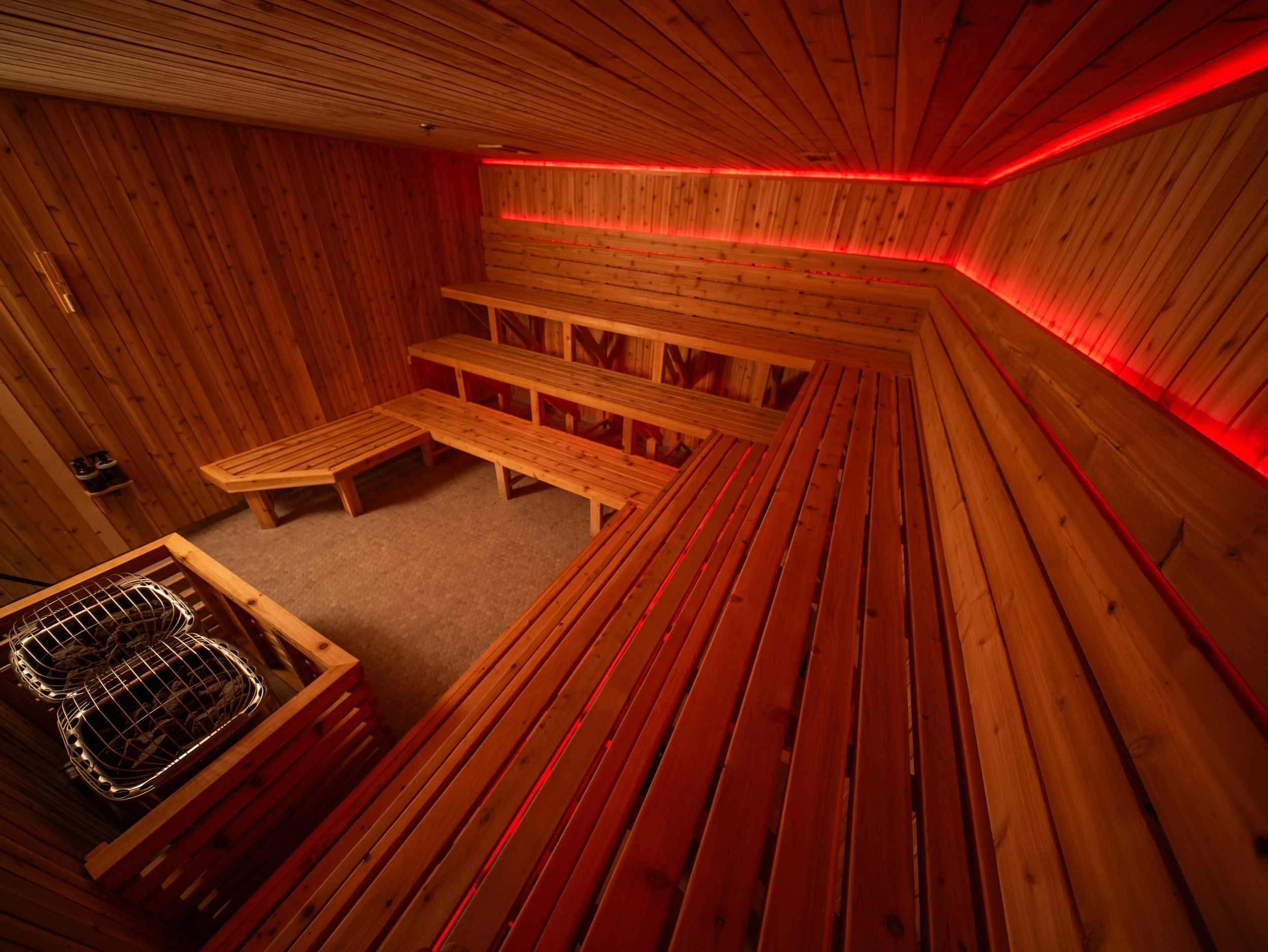 Wide view of a custom-built sauna by Hot Bird Saunas with tiered bench seating and red LED lighting designed for warmth and atmosphere.