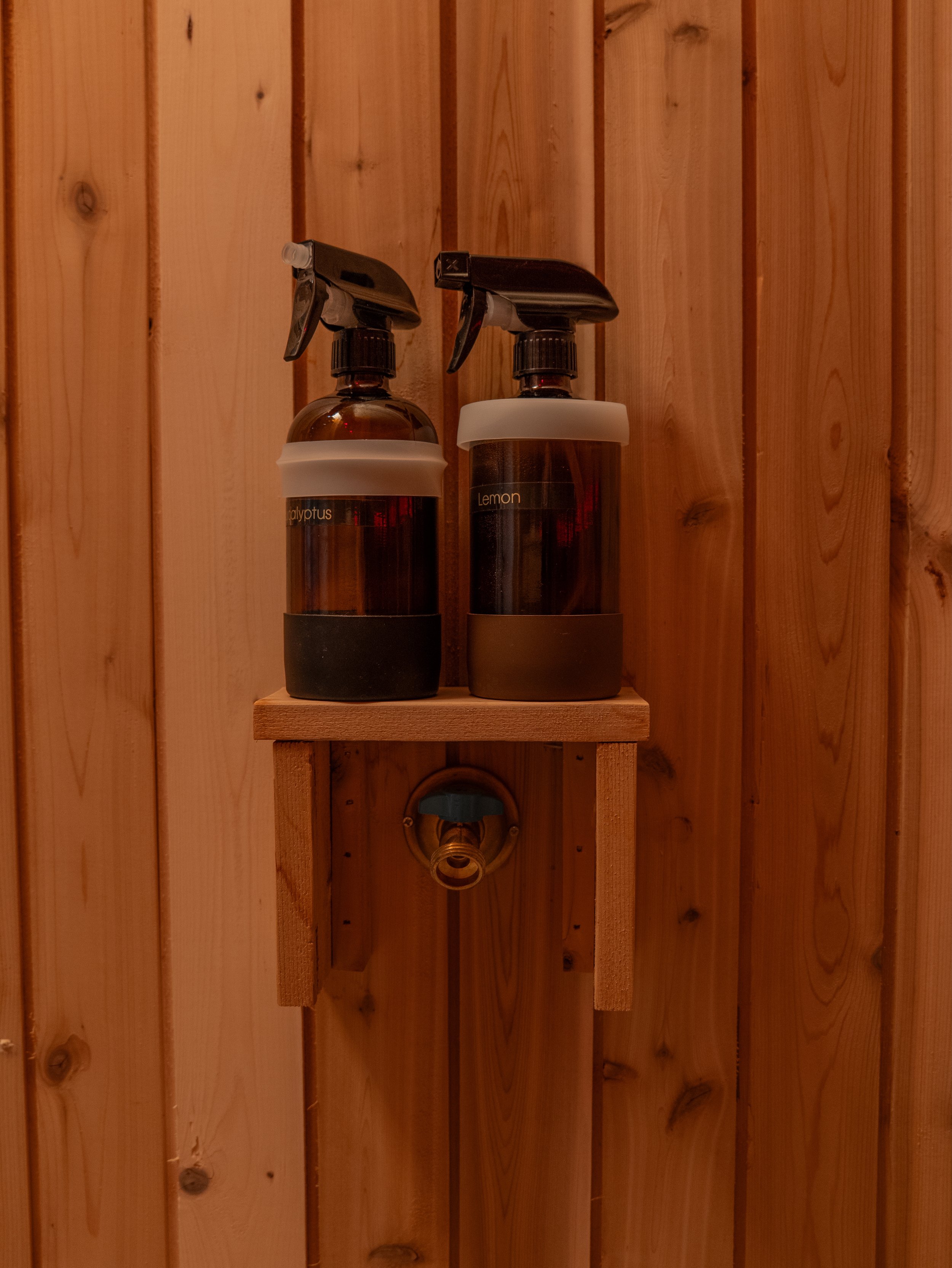 Wooden shelf inside a sauna holding spray bottles for water and essential oils, mounted against wood-paneled walls.