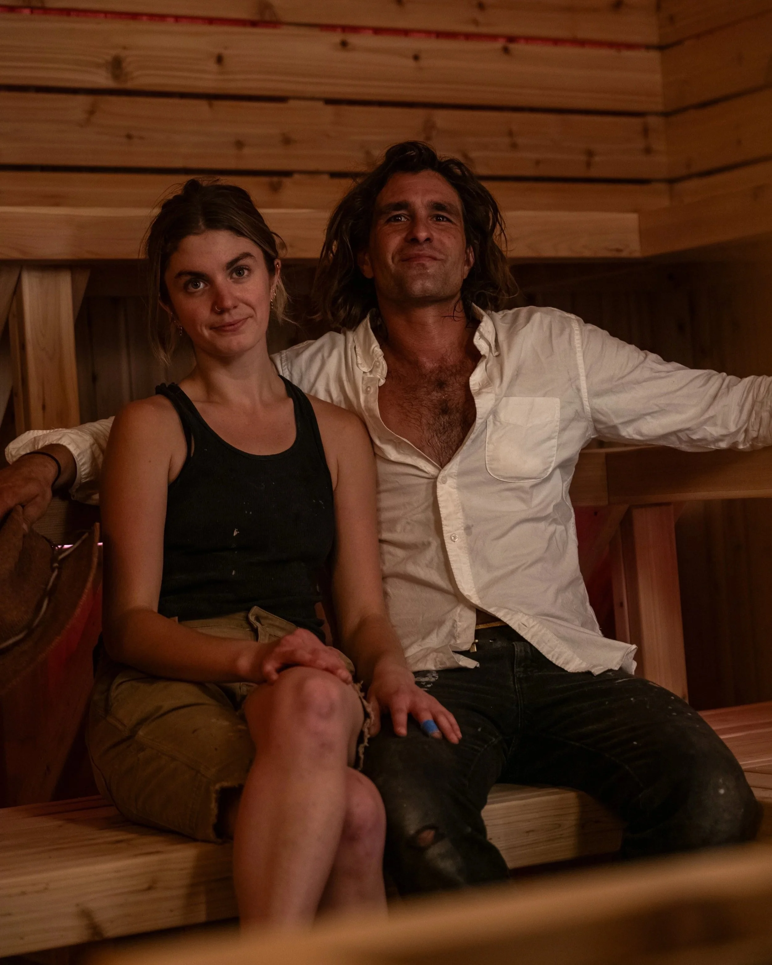 Two people seated on a cedar bench inside a custom-built sauna by Hot Bird Saunas, showcasing warm wood interiors and intimate, human-scaled design.