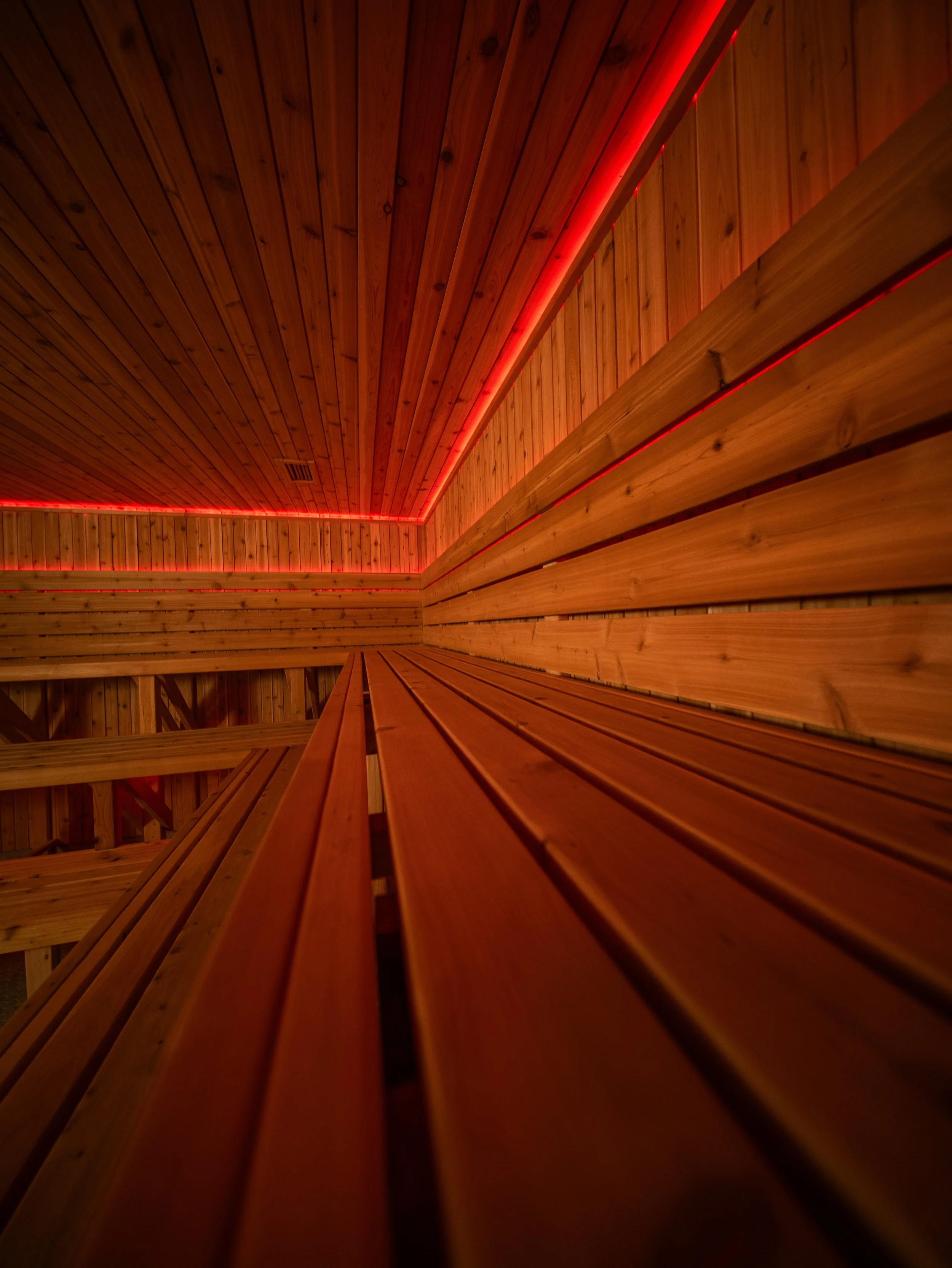 Interior of a custom-built sauna by Hot Bird Saunas featuring horizontal cedar paneling and integrated red LED lighting.