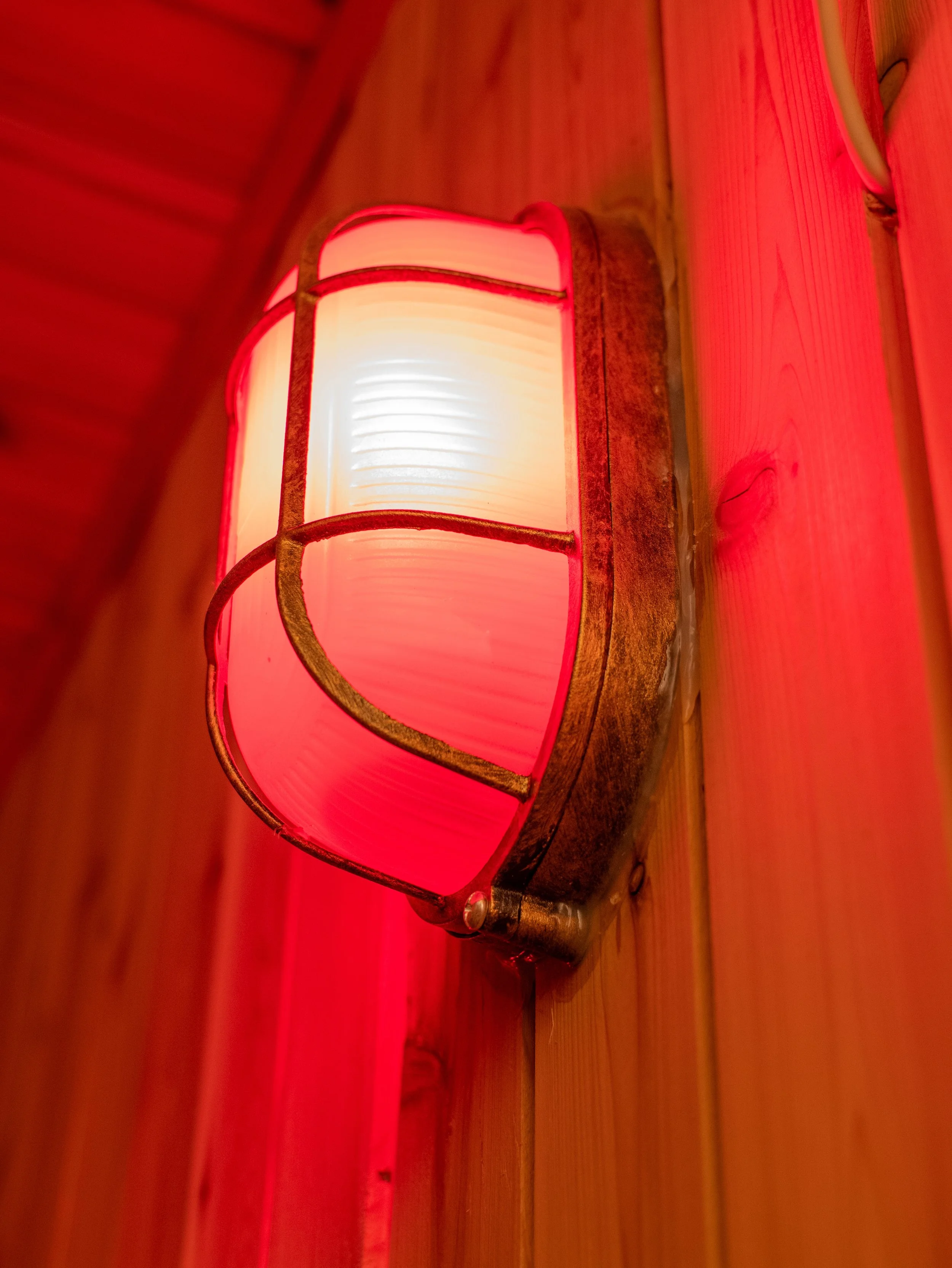 Wall-mounted sauna light with red glass shade installed on a wood-paneled wall inside a custom sauna.