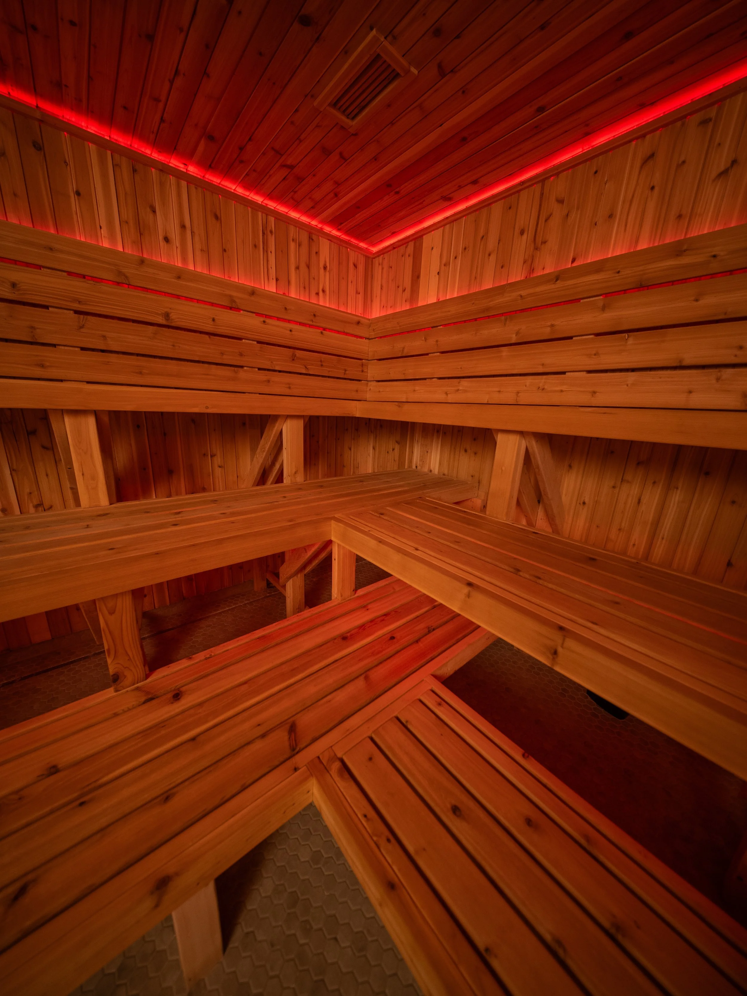 Interior view of a custom sauna with tiered cedar benches and red LED lighting integrated along the ceiling.