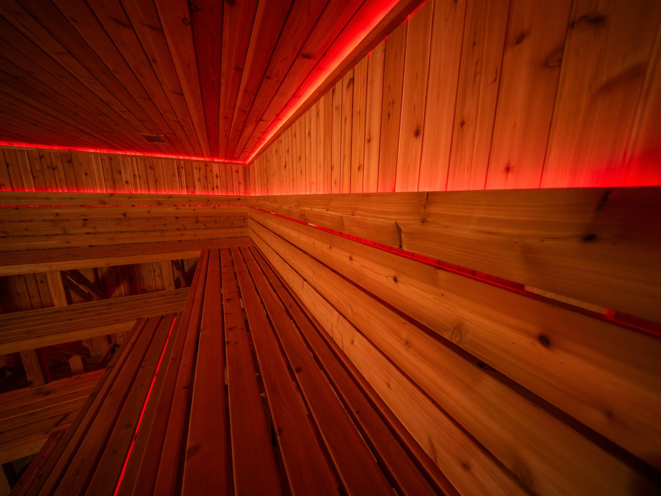 Interior detail of a custom sauna showing red LED lighting integrated along cedar walls.