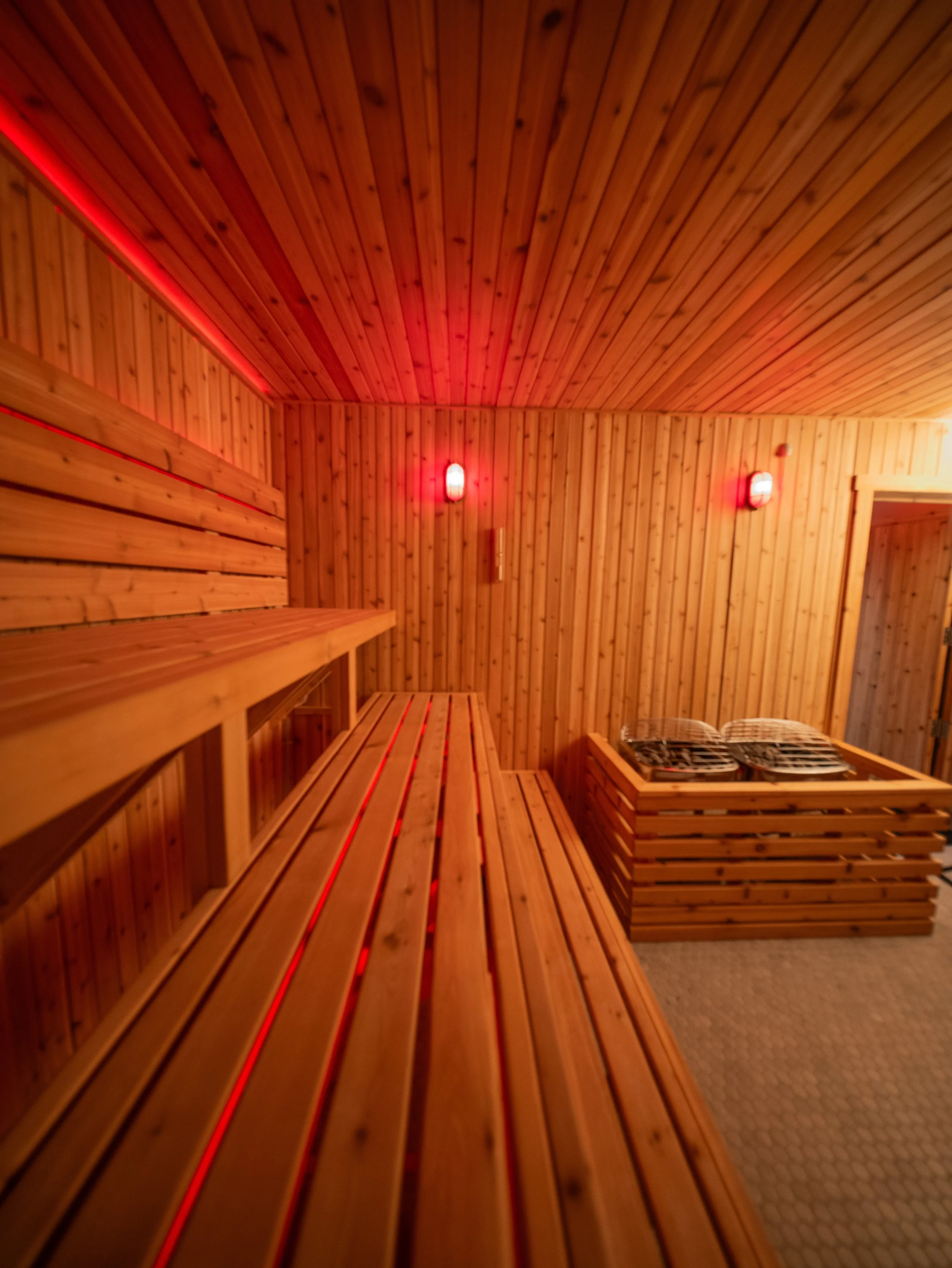 Interior of a custom-built sauna by Hot Bird Saunas featuring cedar benches, warm ambient lighting, and a traditional stone heater.