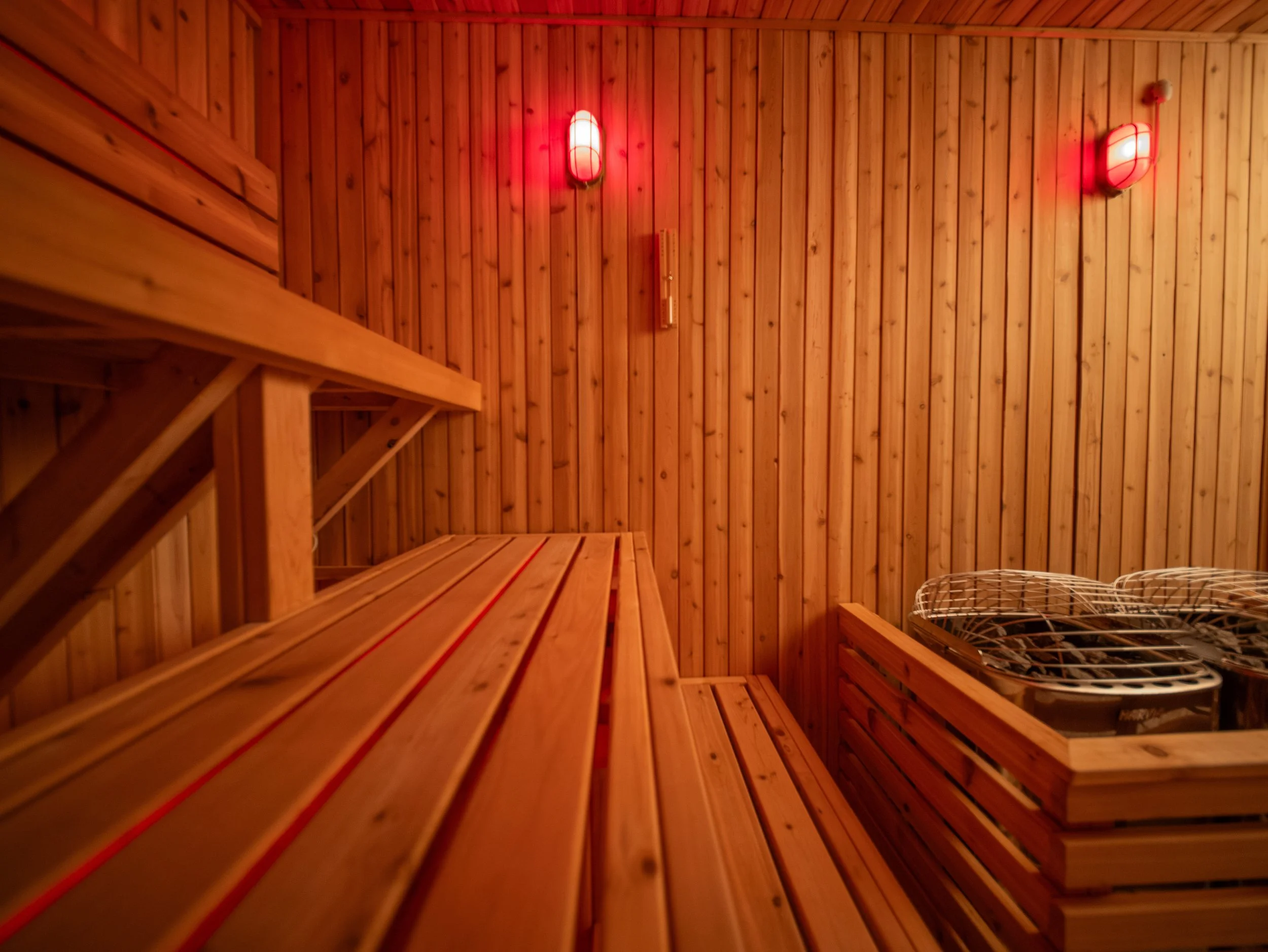 Interior of a custom-built sauna by Hot Bird Saunas featuring cedar bench seating, red ambient lighting, and a traditional stone heater.