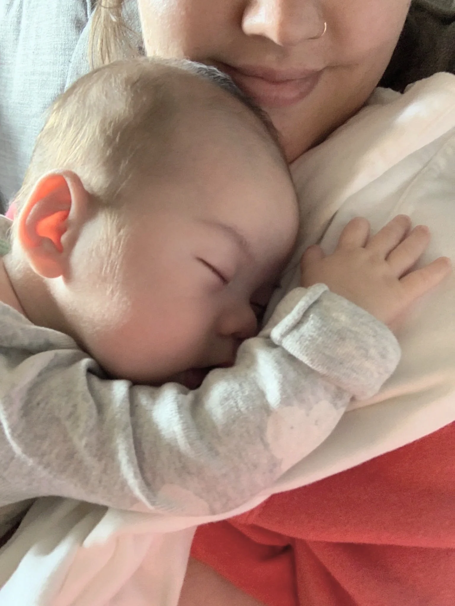 A young child with blond hair sleeping peacefully on a person's chest, with one hand resting on the person's clothes, in a close-up shot showing their face and the person's mouth and nose.