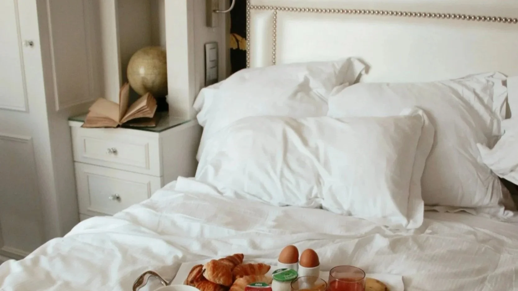 A rumpled bed with breakfast on a tray and an open book, the scene of a day spent reading in bed