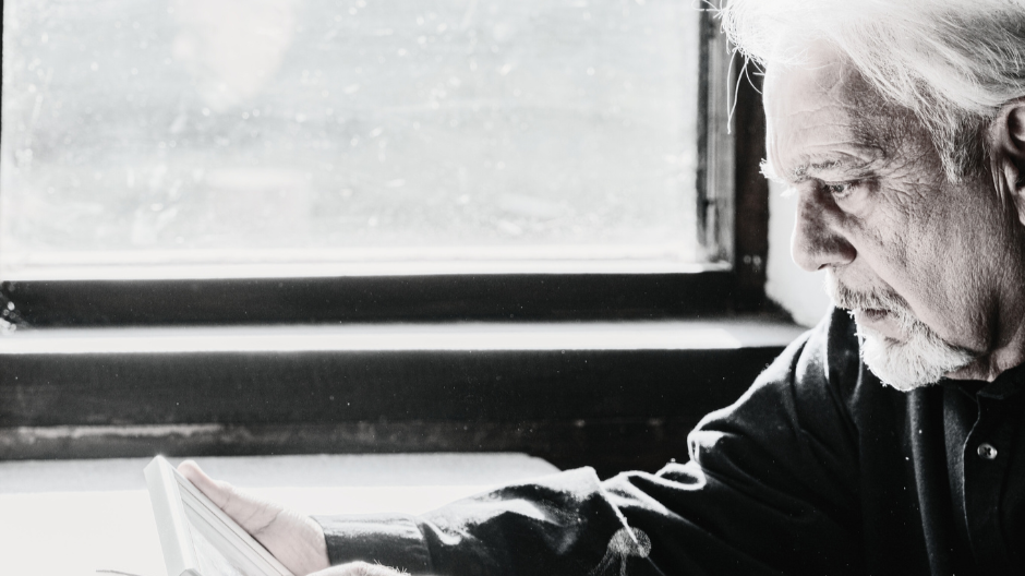 Mature man sitting by a window holding a photo frame and reflecting on memories in later life