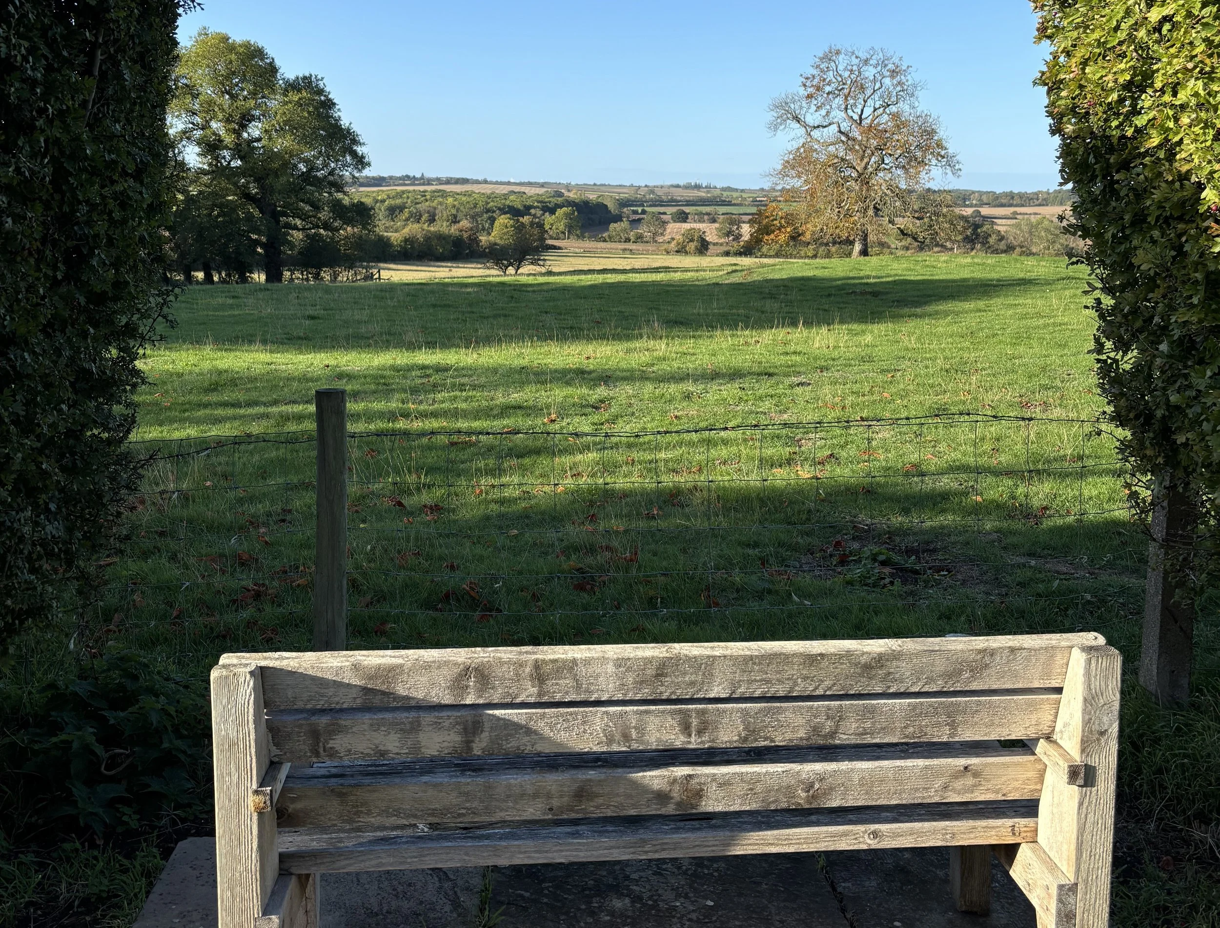 A single wooden bench looking over an open green field in Little Gidding
