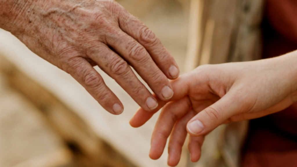 An older hand and a younger hand, fingertips just parting, letting go.