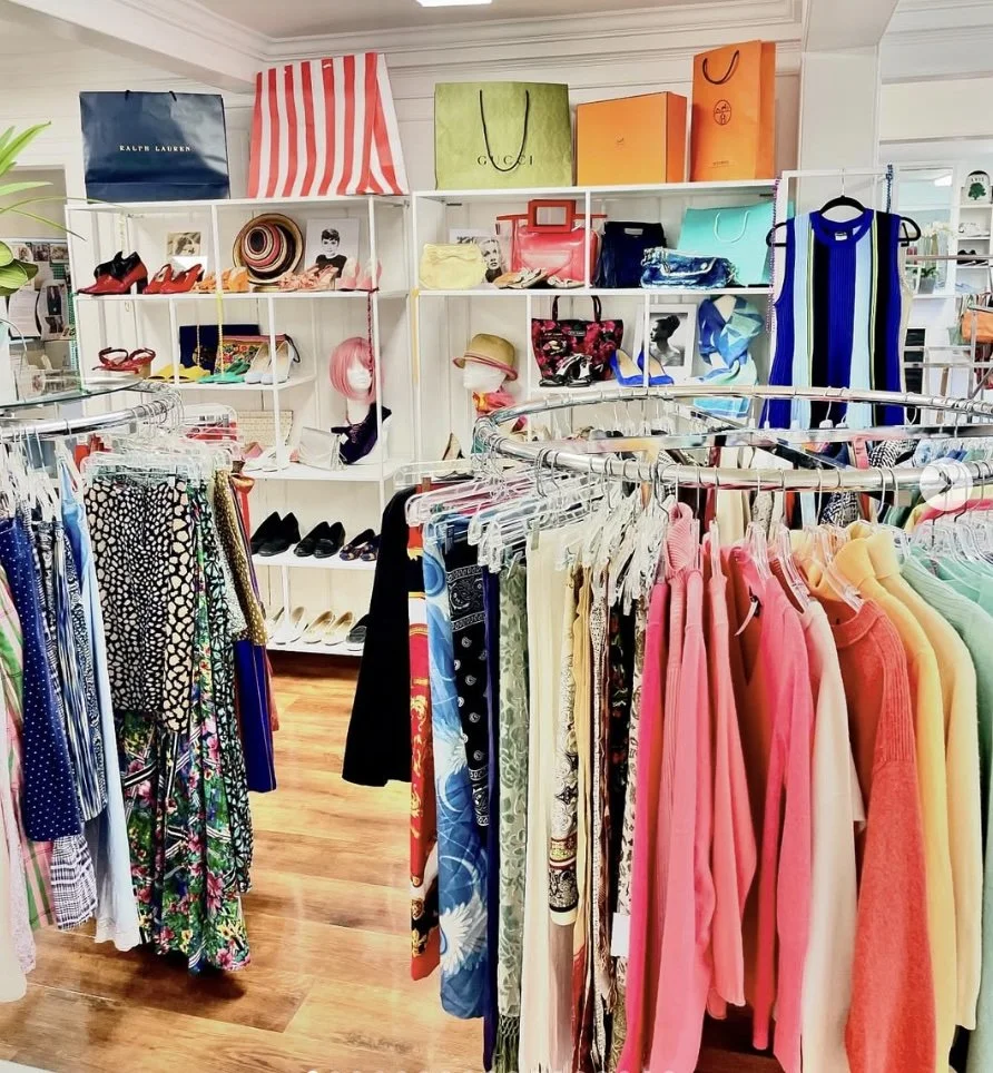Clothing store with racks of colorful dresses, handbags, shoes, and shopping bags on shelves.