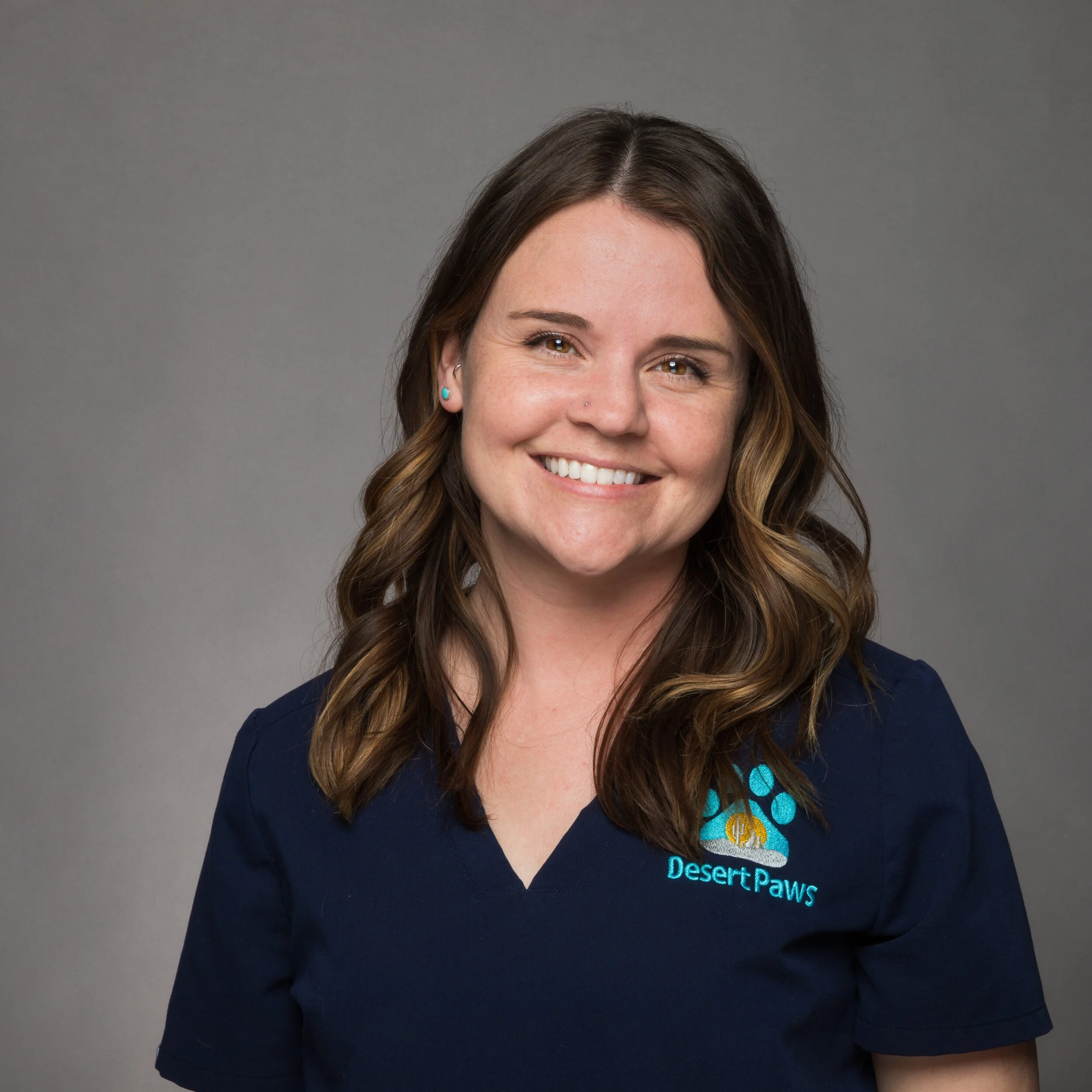 Smiling portrait of a woman wearing vet practice scrubs against a gray background.