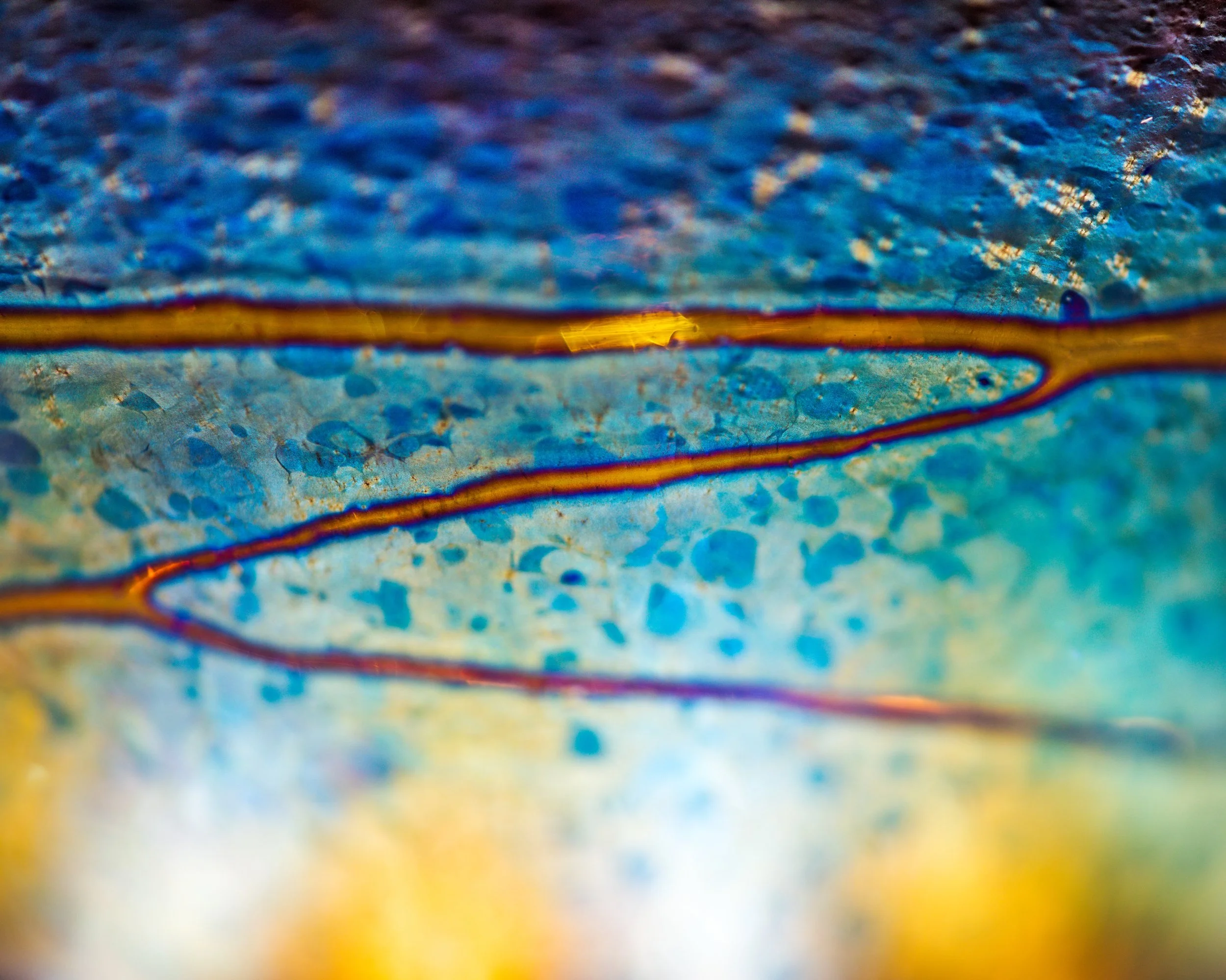 A highly macro photography close-up of colorful glass and surface showing vibrant colors and intricate textures.