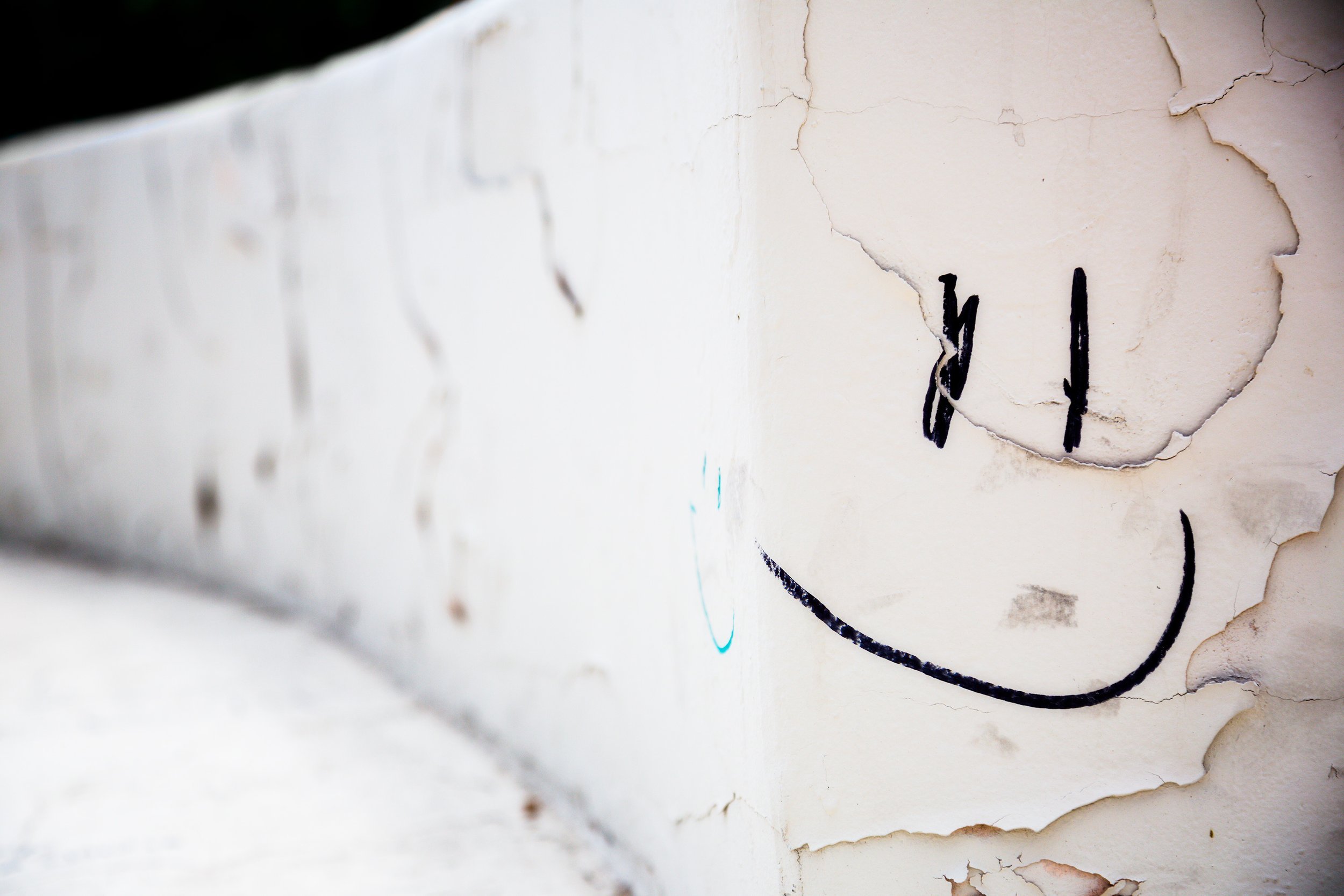 Close-up of a peeling white wall with graffiti of a black smiley face in downtown Tucson, Arizona.