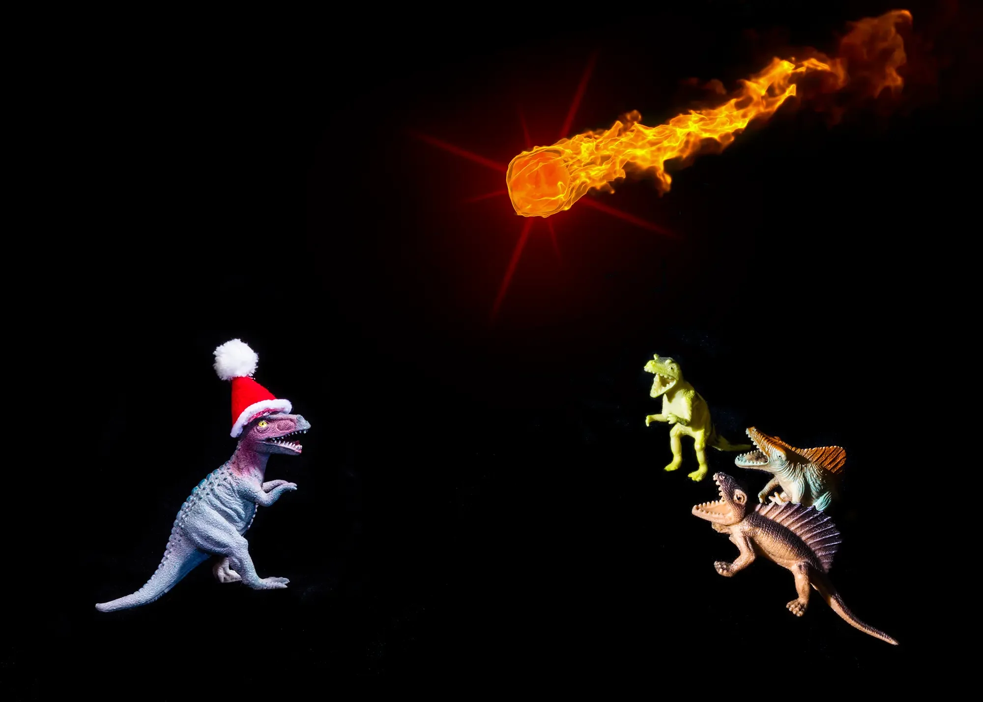 Toy T-Rex in Santa hat watching a flaming comet streak overhead while three other dinosaurs react in panic in the background, against a dark studio sky