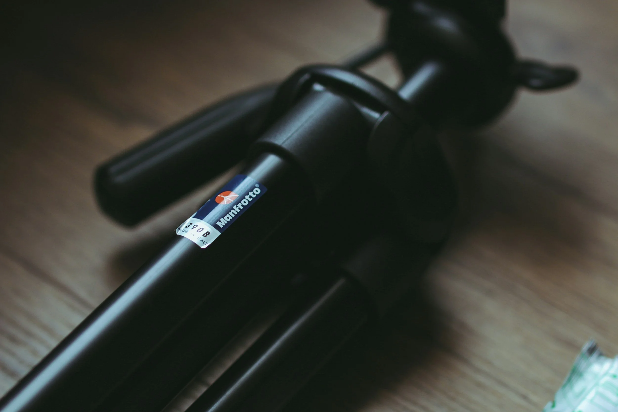 Close-up of a black Manfrotto tripod leg with a label, on a wooden surface.