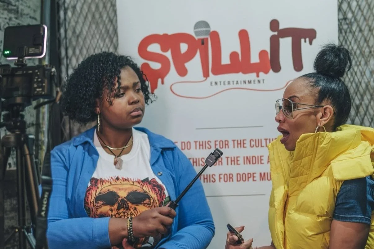 Two women having a conversation during an interview in front of a banner with the word 'Splatt' in red letters.