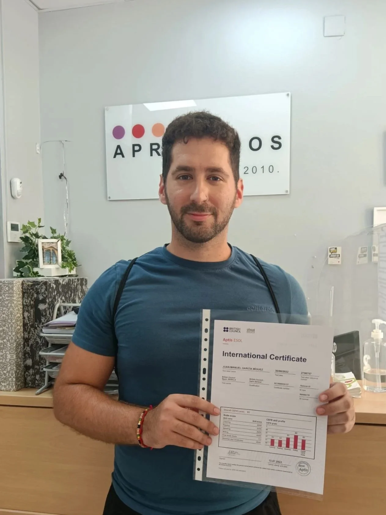 Hombre con barba con camisa azul sosteniendo certificado internacional en una oficina.