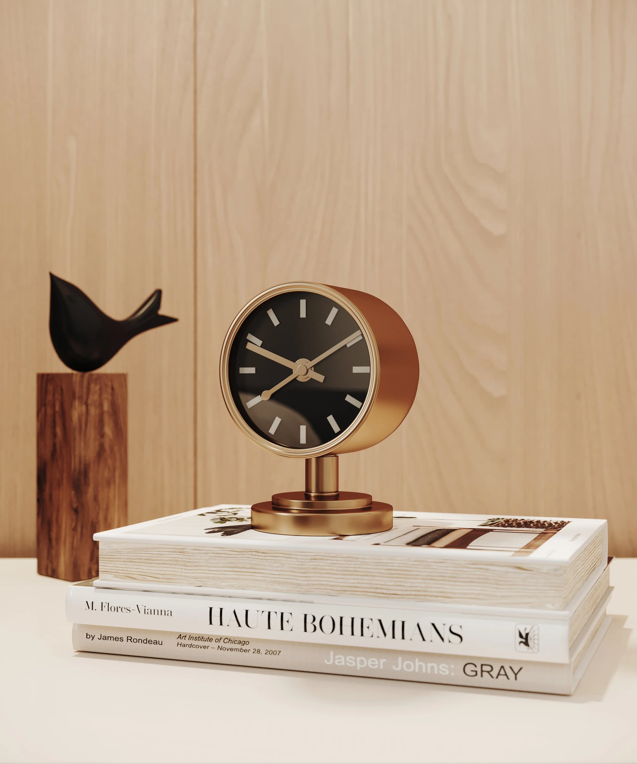 A black and gold clock with a black face and white hands, placed on top of a stack of three art books, with a dark bird sculpture on a wooden pedestal in the background, against a wood-paneled wall.