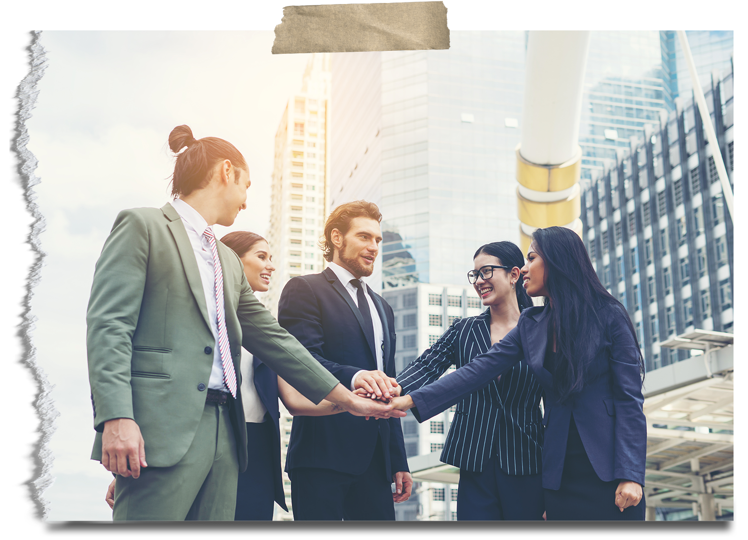 Five diverse businesspeople in suits cheer and place hands together in a cityscape with tall modern buildings.
