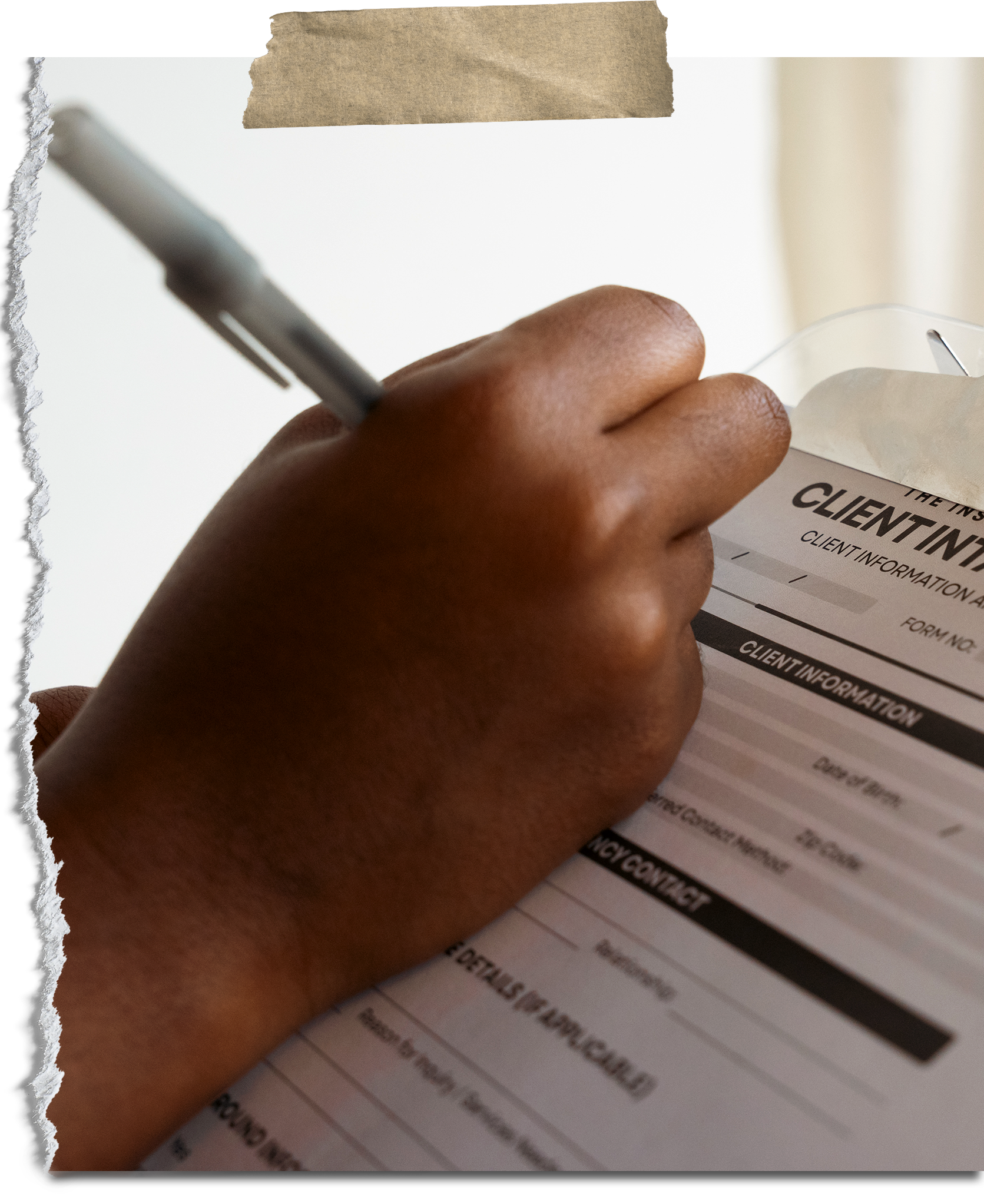 Close-up of a person's hand filling out a client information form on a clipboard with a pen