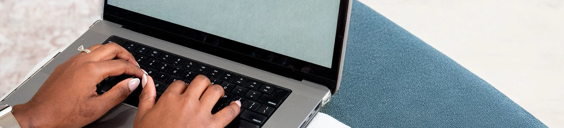 Hands typing on a laptop keyboard placed on a table with a blue and white surface.