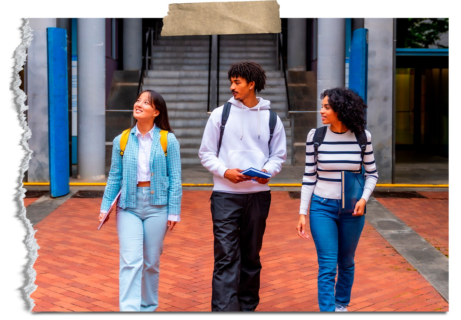 Three diverse students walking and talking outside a modern building with brick pavement, stairs, and glass doors, carrying notebooks and backpacks.