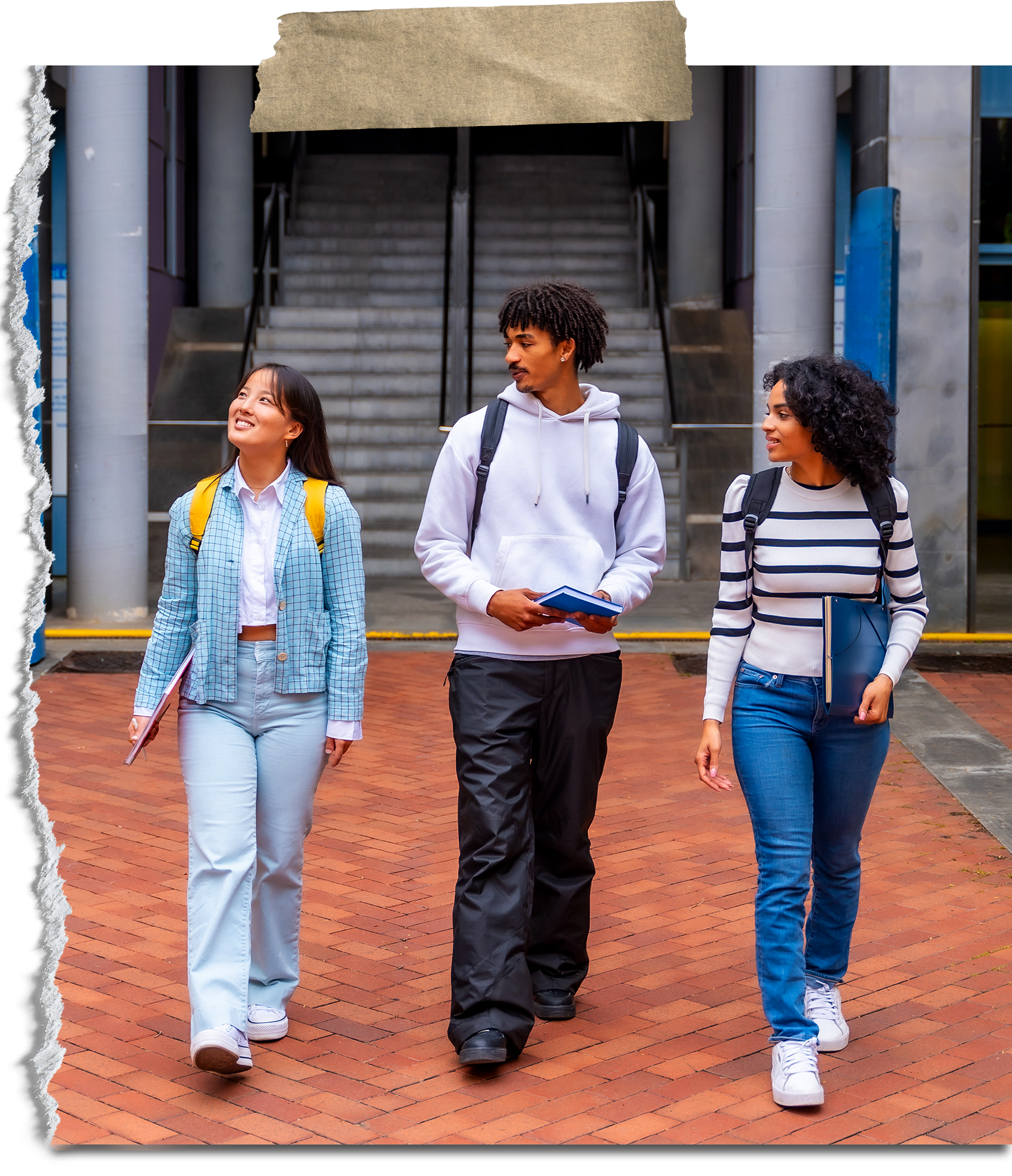 Three students walking on a college campus, talking and holding notebooks.