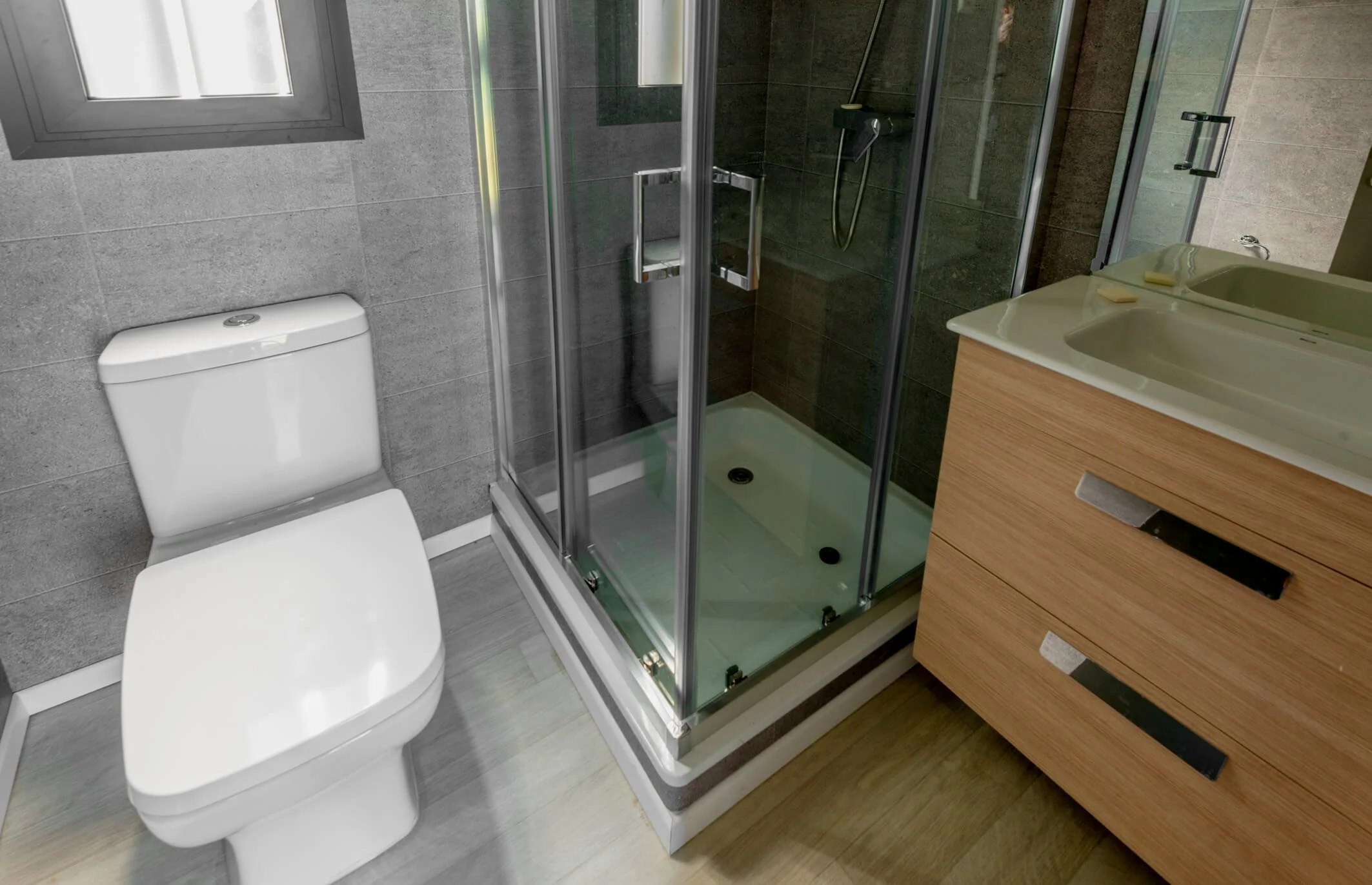 Baño con inodoro, ducha con puertas de cristal y lavabo con mueble de madera.