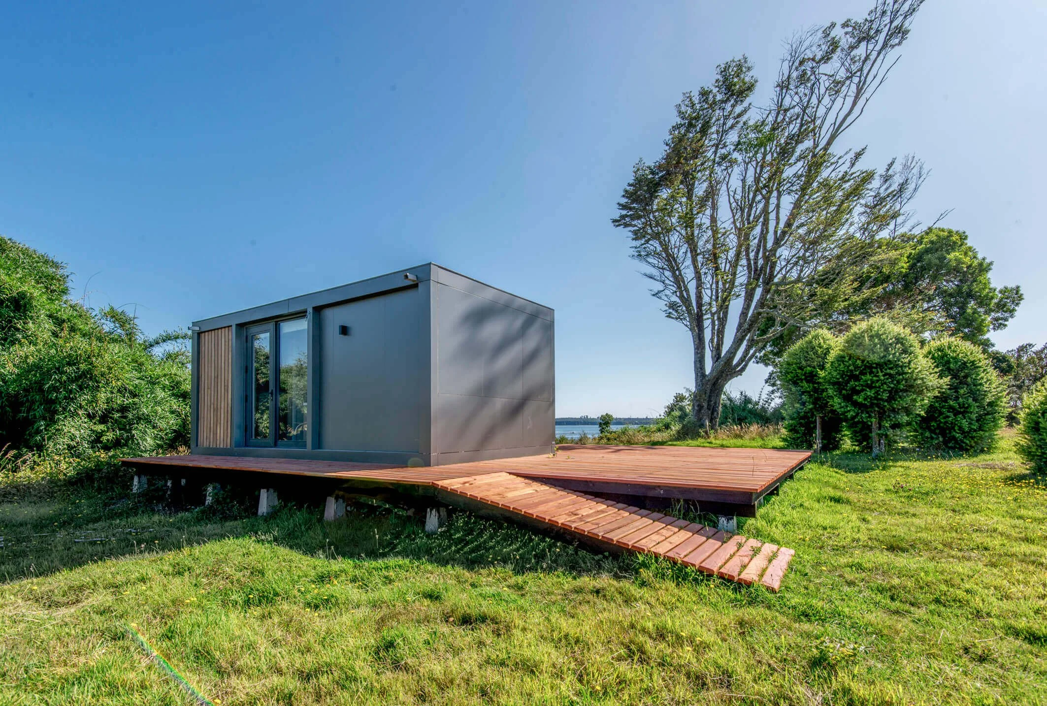 Casa moderna de una planta en un entorno natural con árboles y césped, en un día soleado con cielo despejado.