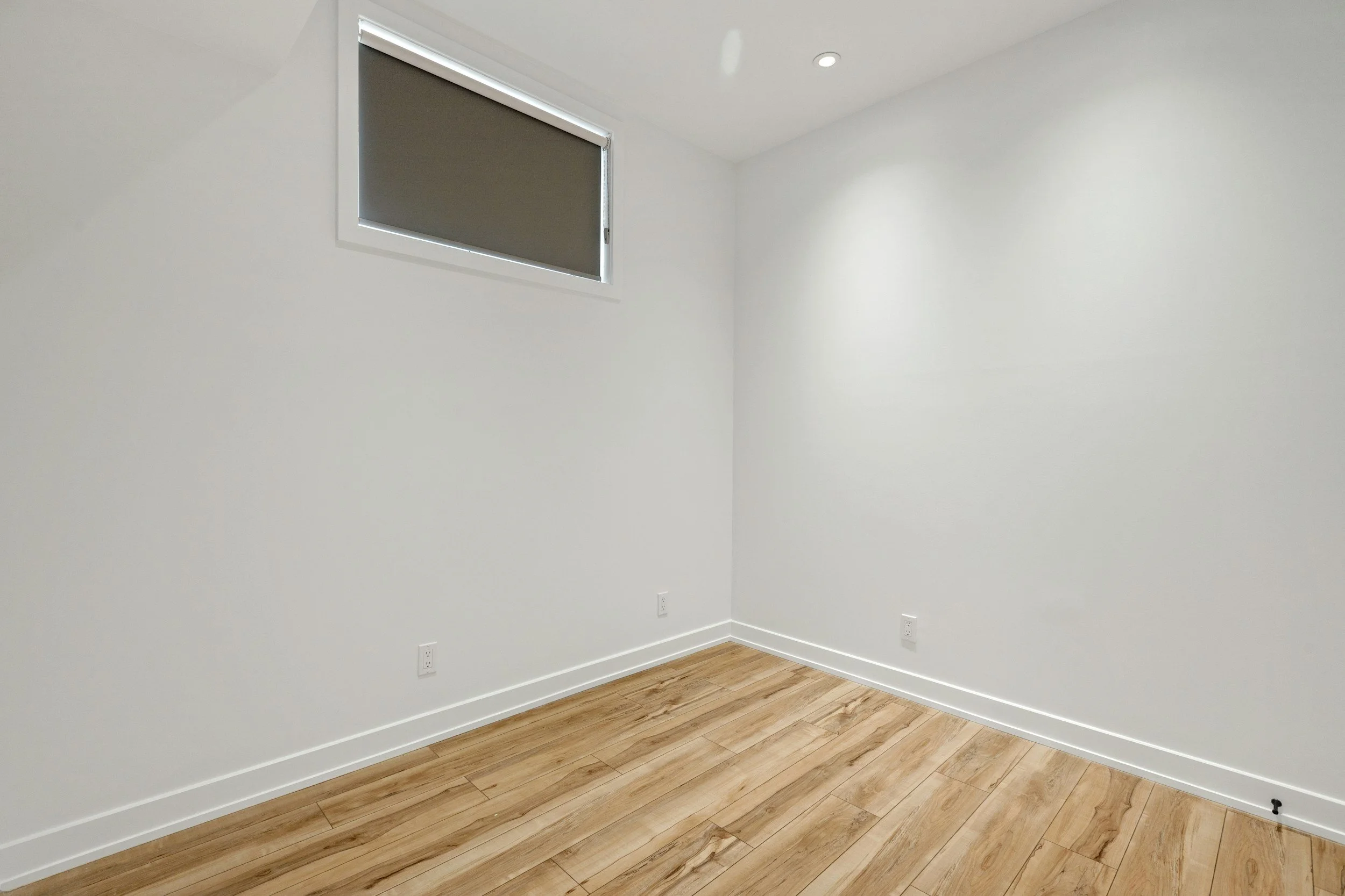 Empty room with white walls, a small window, and wooden flooring.