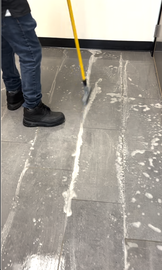Person cleaning tiled floor using a mop with soap and water, with visible soap suds and streaks.