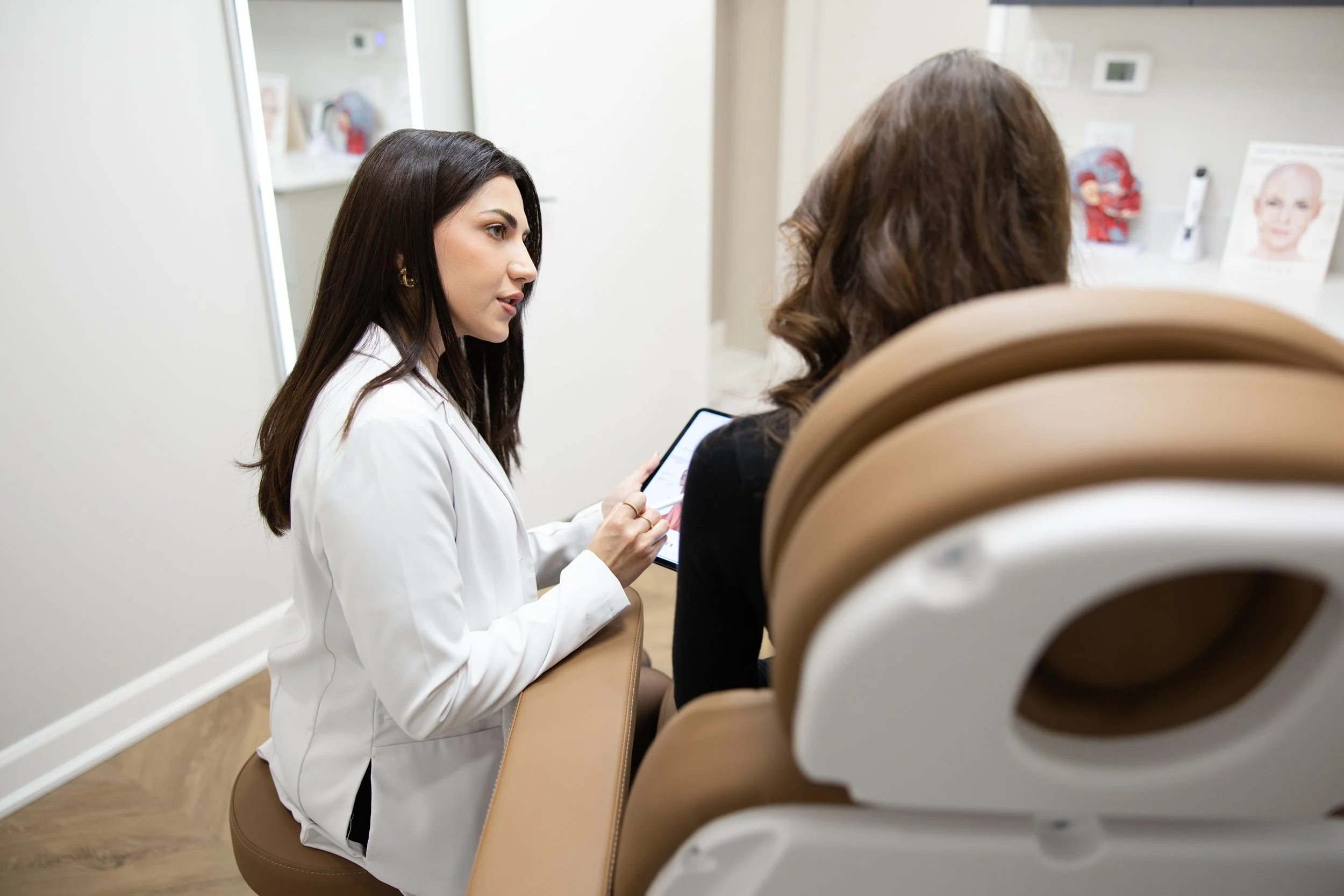 A female doctor explains medical information to a patient in a clinic, using a tablet device.