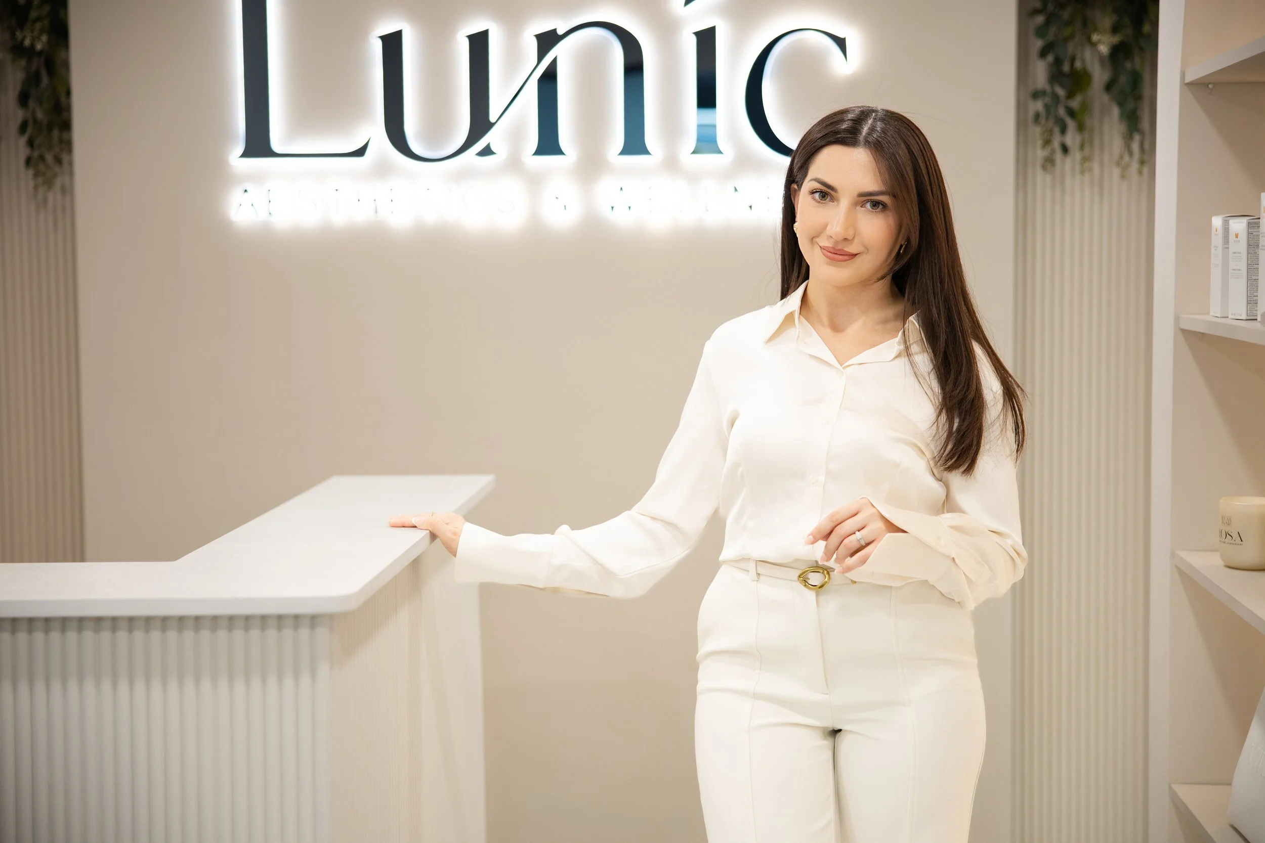 A woman standing at a reception desk in front of a sign that says 'Luna' in a spa or cosmetic clinic.