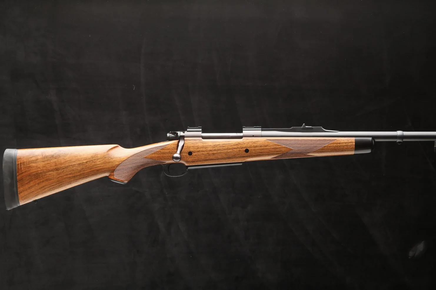 A rifle with a wooden stock and metal barrel against a black background.