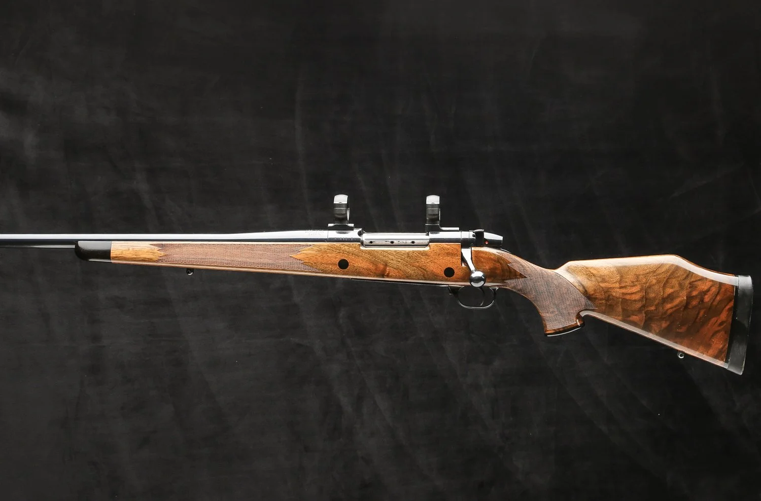 A bolt-action hunting rifle with a wooden stock and black metal components, lying horizontally on a black surface.