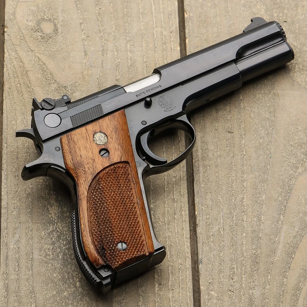 A semi-automatic pistol with a black metal body and wooden grips lying on a wooden surface.