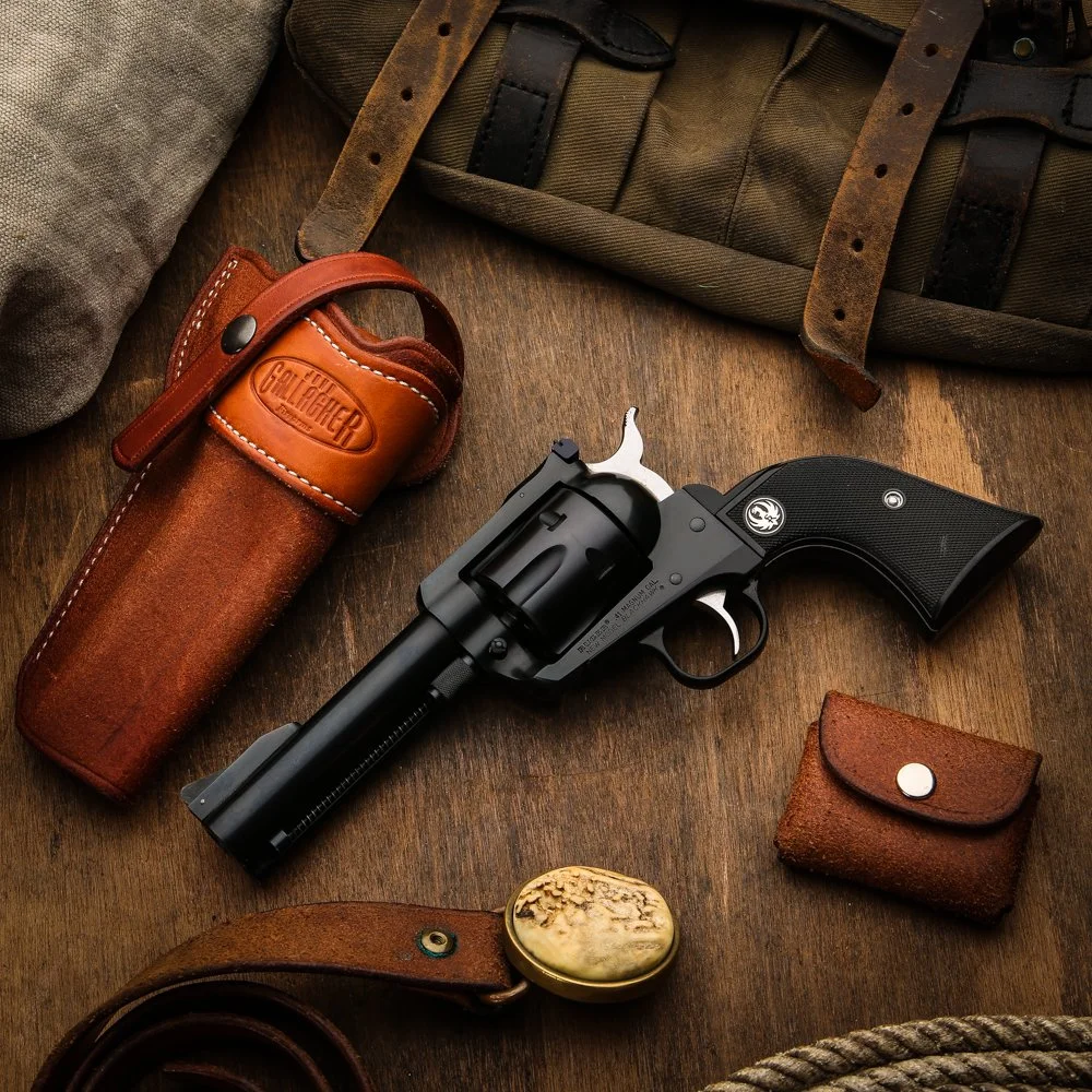 A revolver handgun and various leather and fabric accessories on a wooden surface, including a holster, wallet, and a small pouch.