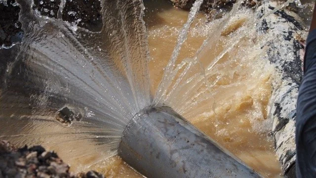 Water pouring out of a broken, large metal pipe into muddy water.