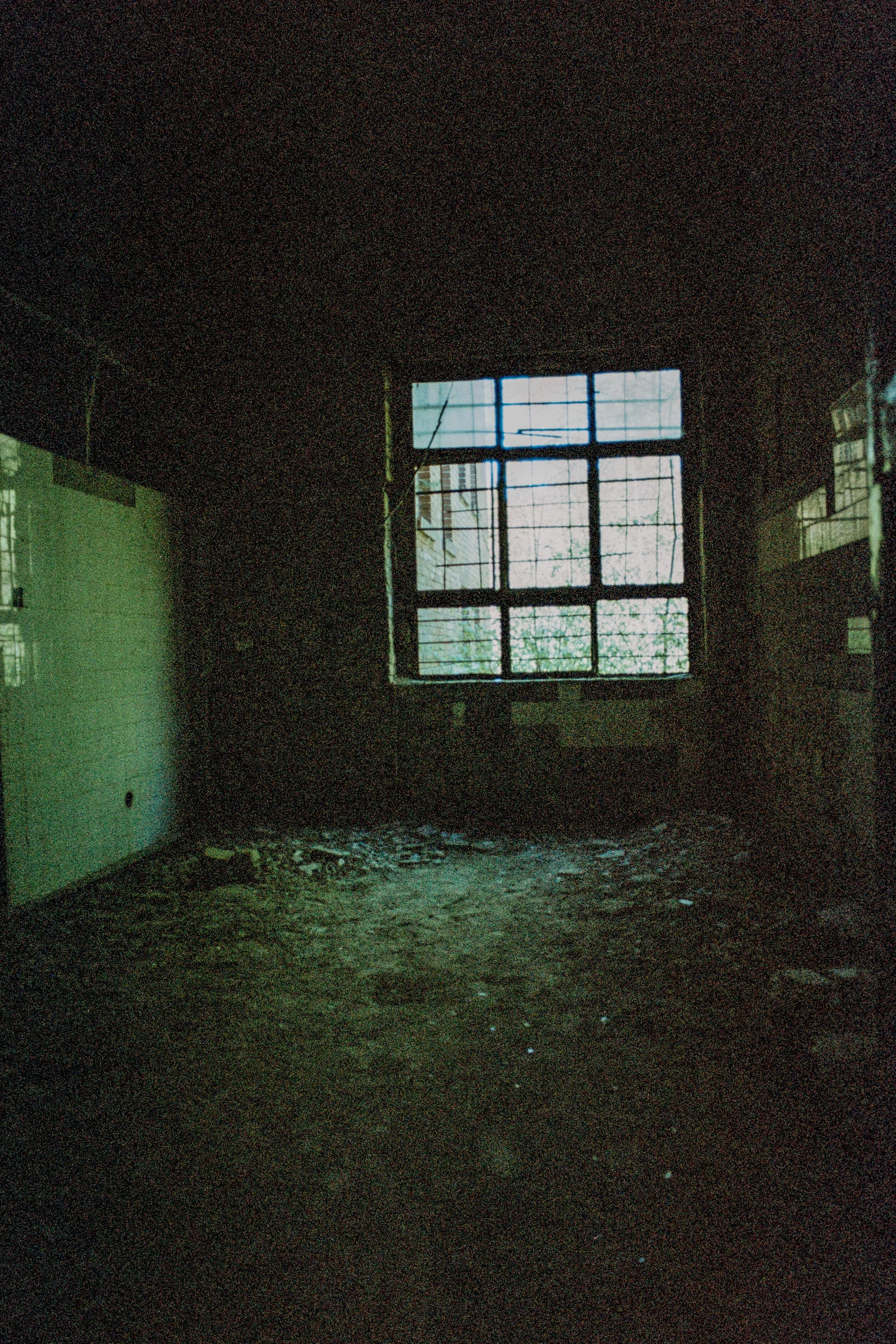 Verlassener Raum mit schmutzigem Boden und einem alten Fenster mit Gitter, viel Dunkelheit im Raum.