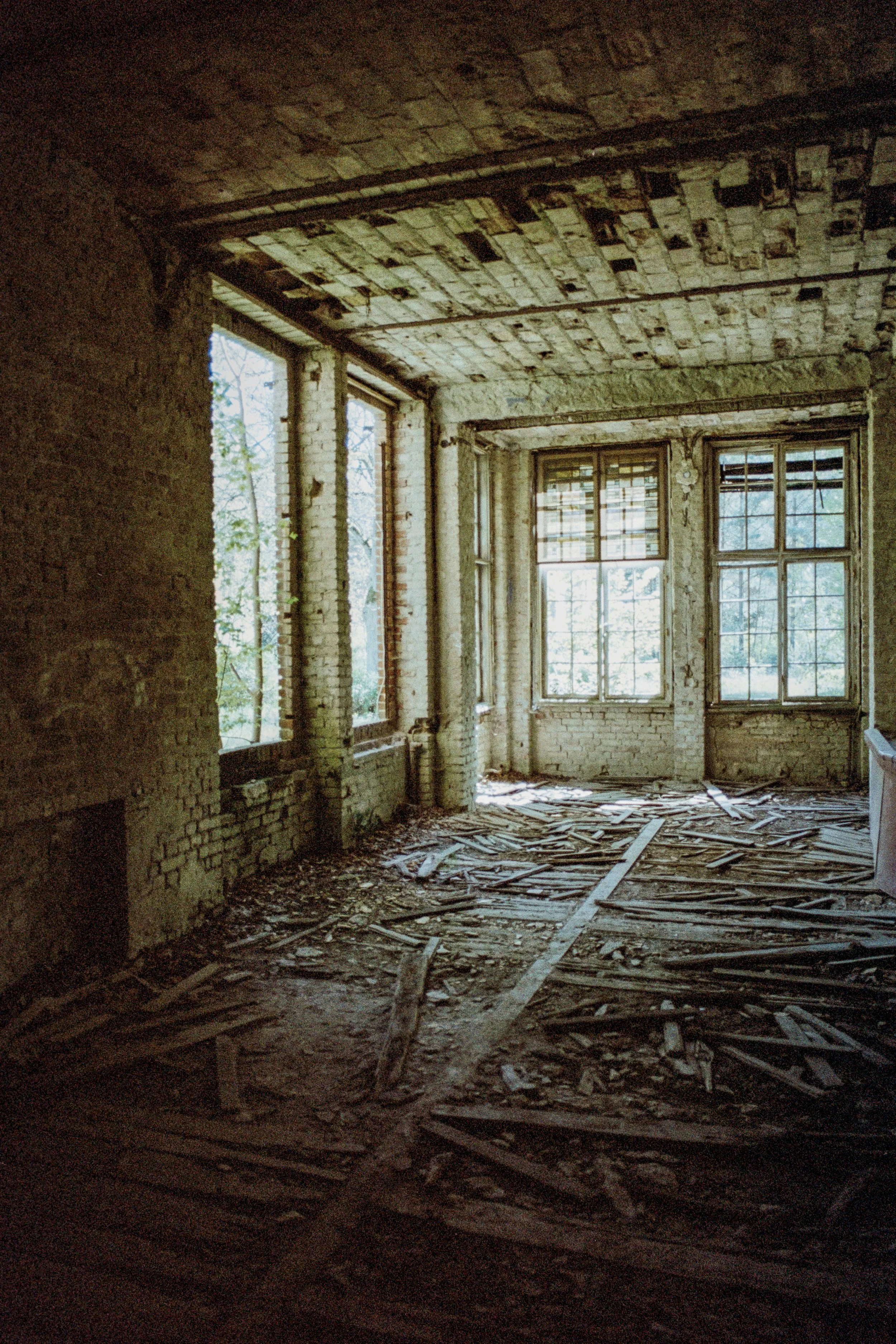 Verlassener, verfallener Raum mit zerbrochenen Dielen und alten Fenstern, viel Licht strömt durch die Fenster.