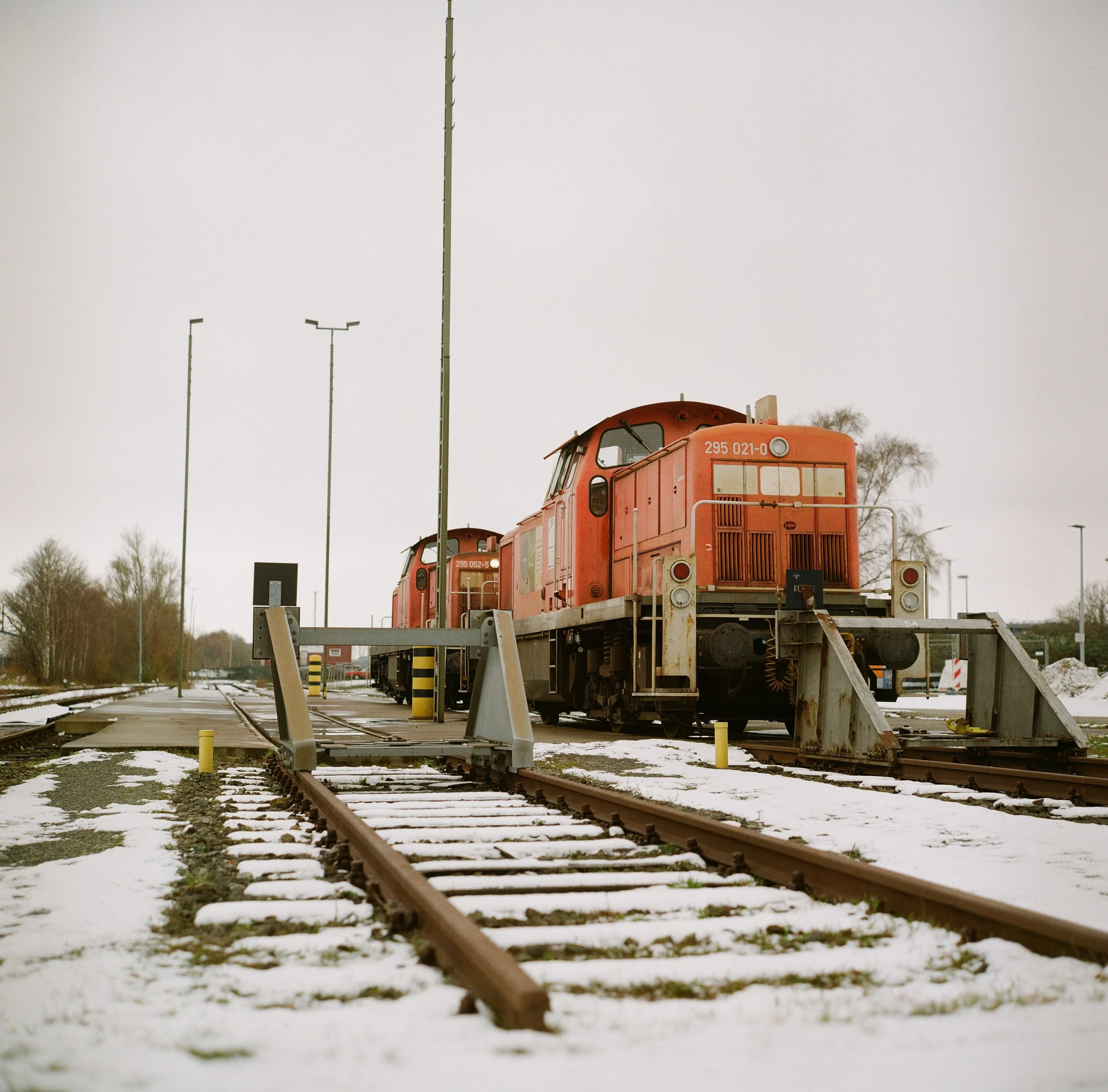 Zwei rote Bahndrehgestelle auf stillgelegten Gleisen im Winter mit Schneeresten und darüber liegenden Laternen.