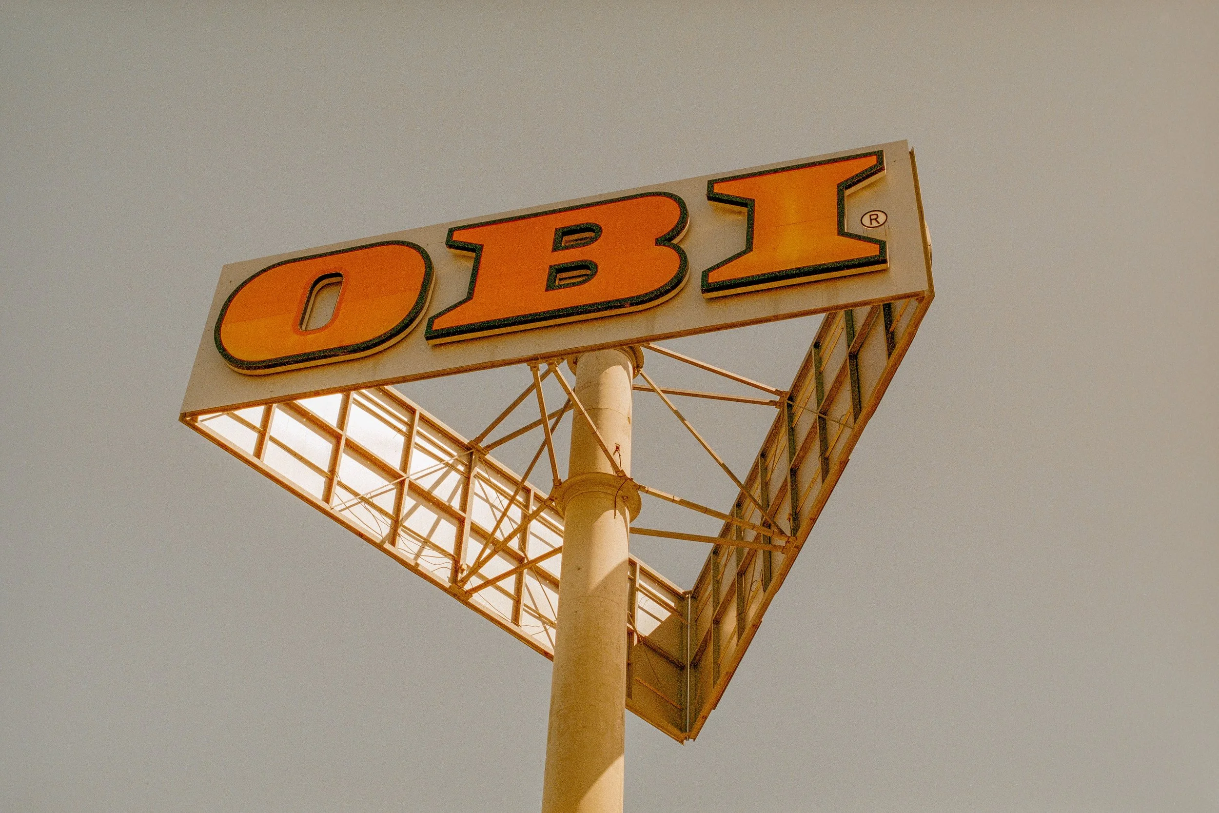Schild mit der Aufschrift 'OBI' auf einem großen weißen Pfeiler gegen den Himmel.