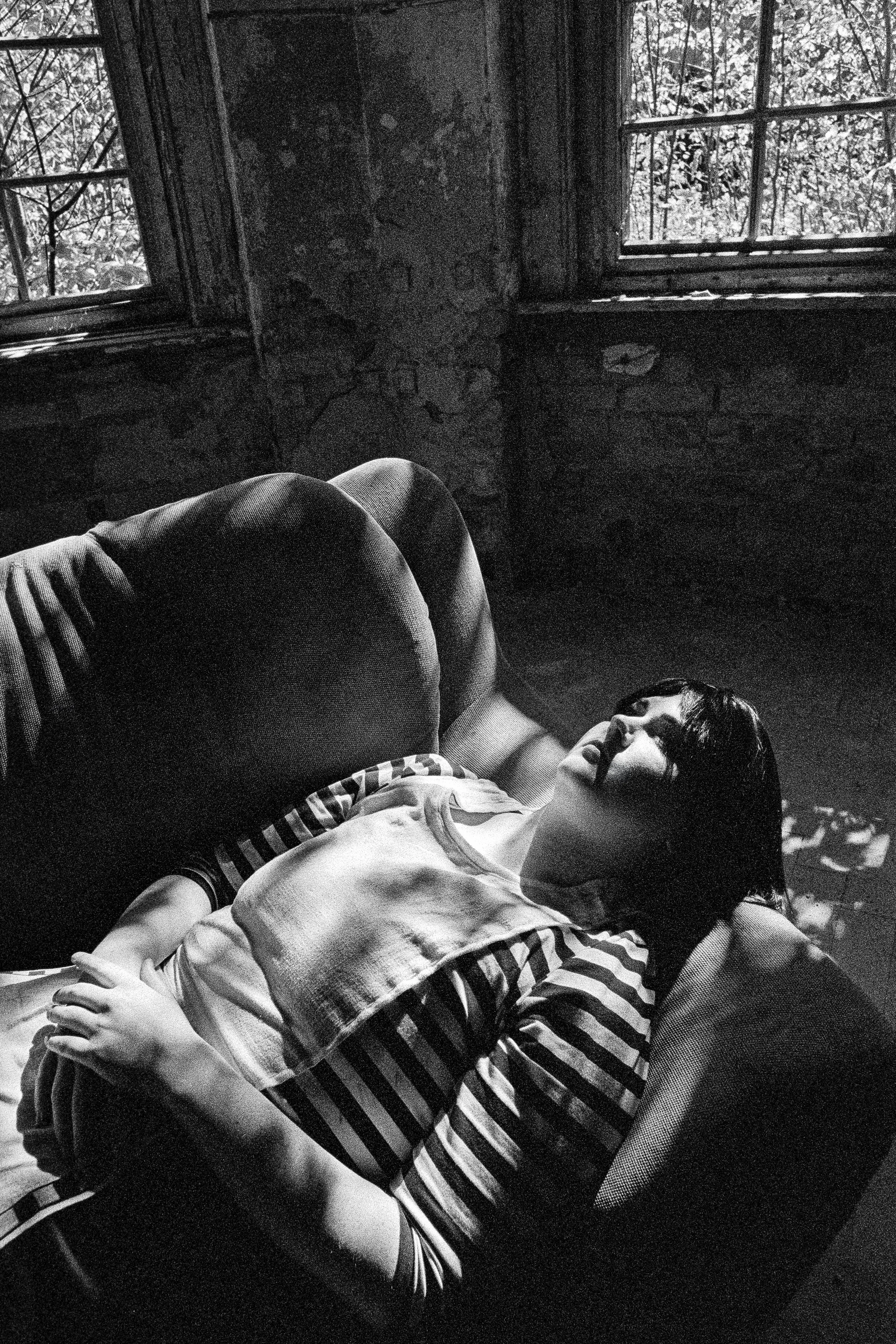 Frau liegt entspannt auf einer Couch in einem alten, dunklen Raum mit großen Fenstern, durch die Tageslicht einfällt.