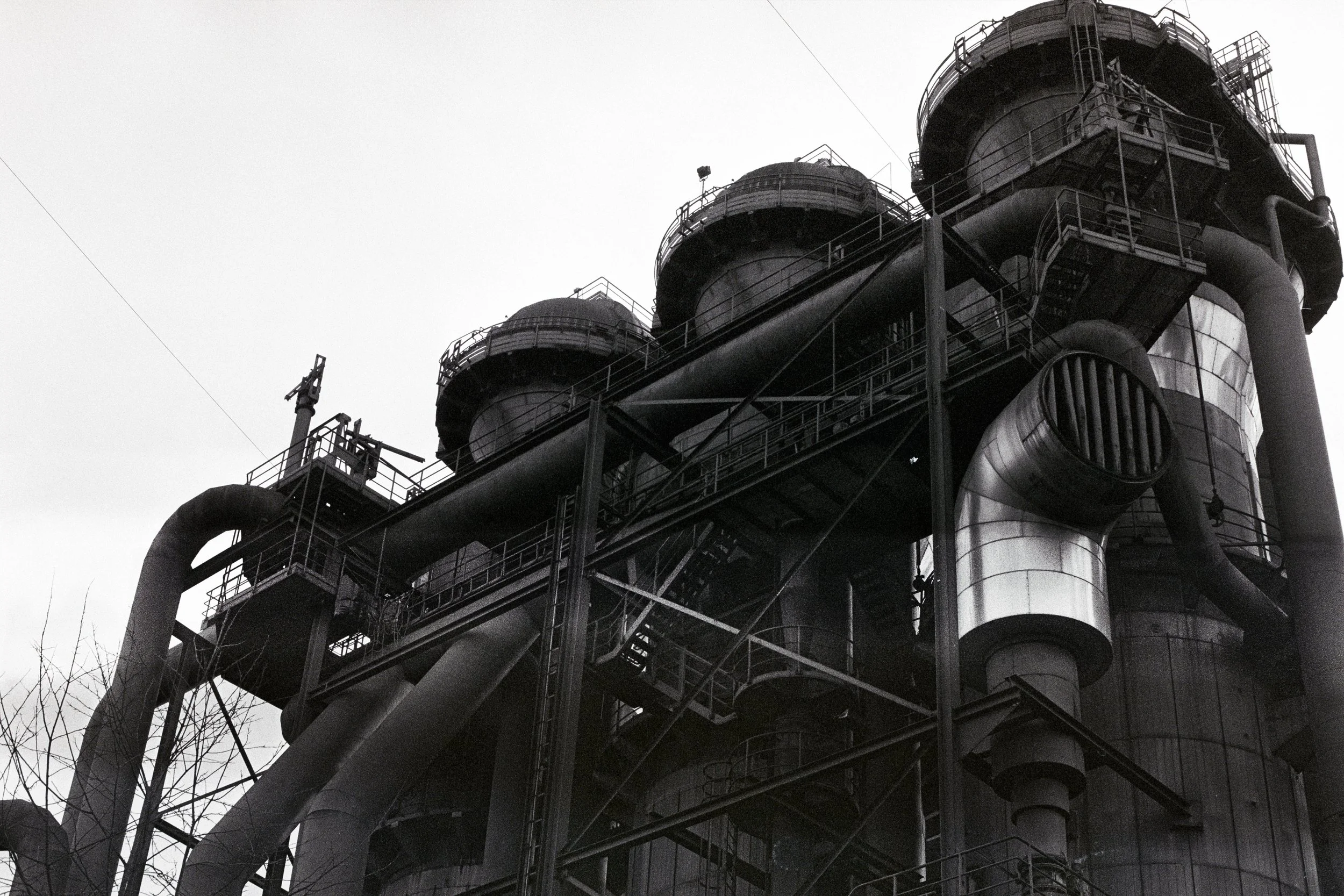 Schwarz-weiß-Bild eines Industriegebäudes mit Rohren, Leitern und Plattformen aus Metall.