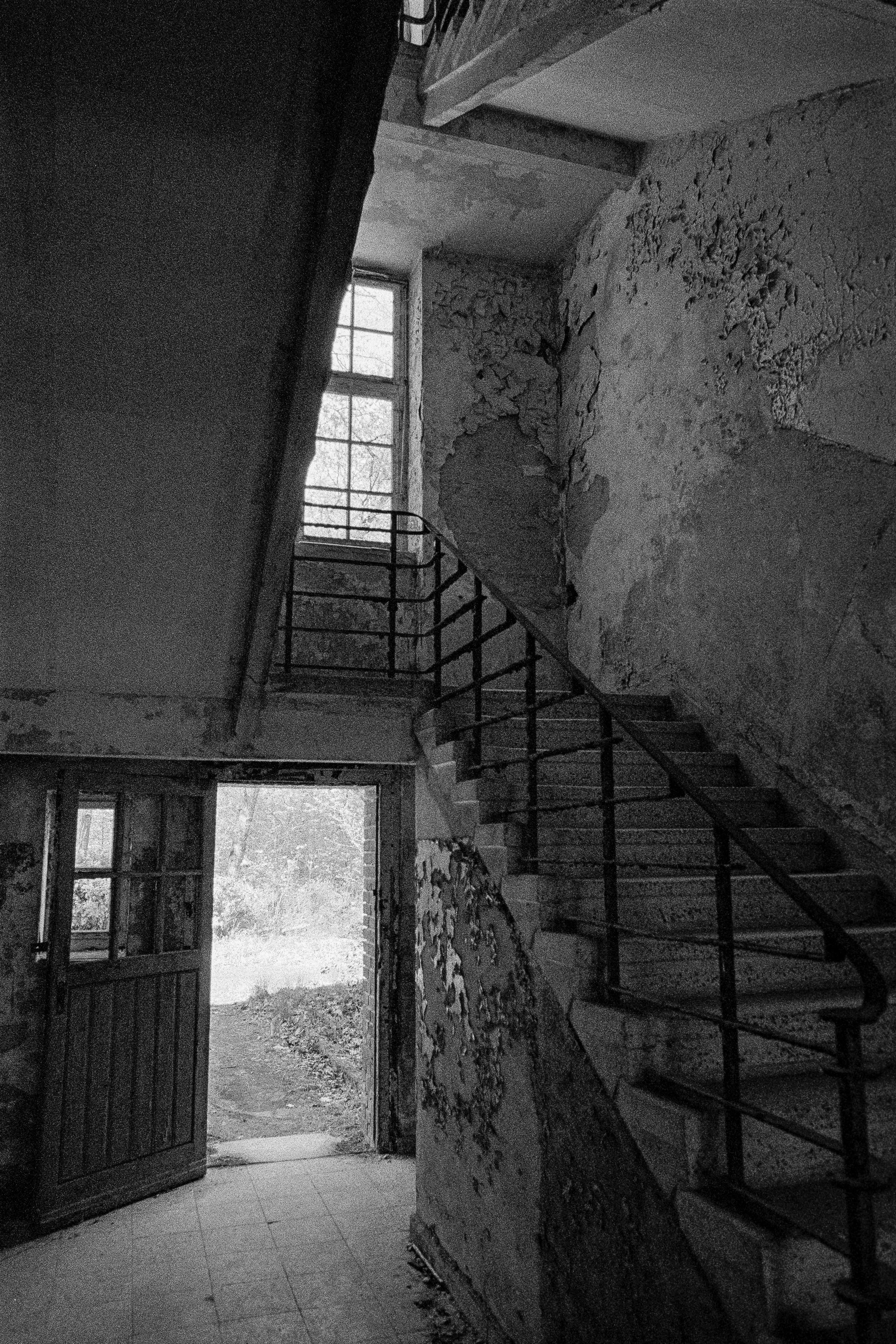 Verlassene, verfallene Treppe in einem alten Gebäude mit zerbröckelnder Wand und offenem Eingang ins Freie.